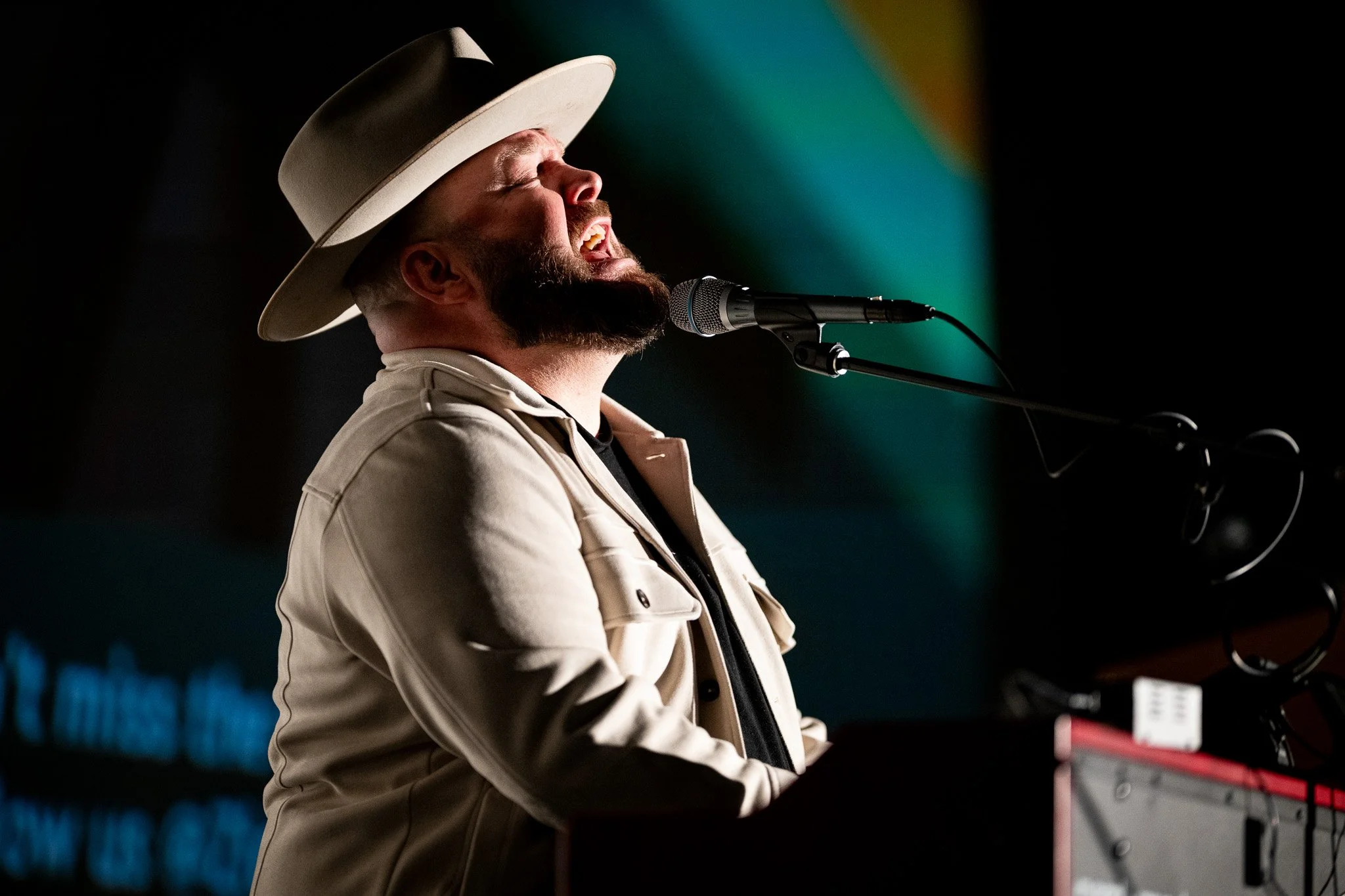 Singer performing on stage with microphone, wearing a hat and jacket.