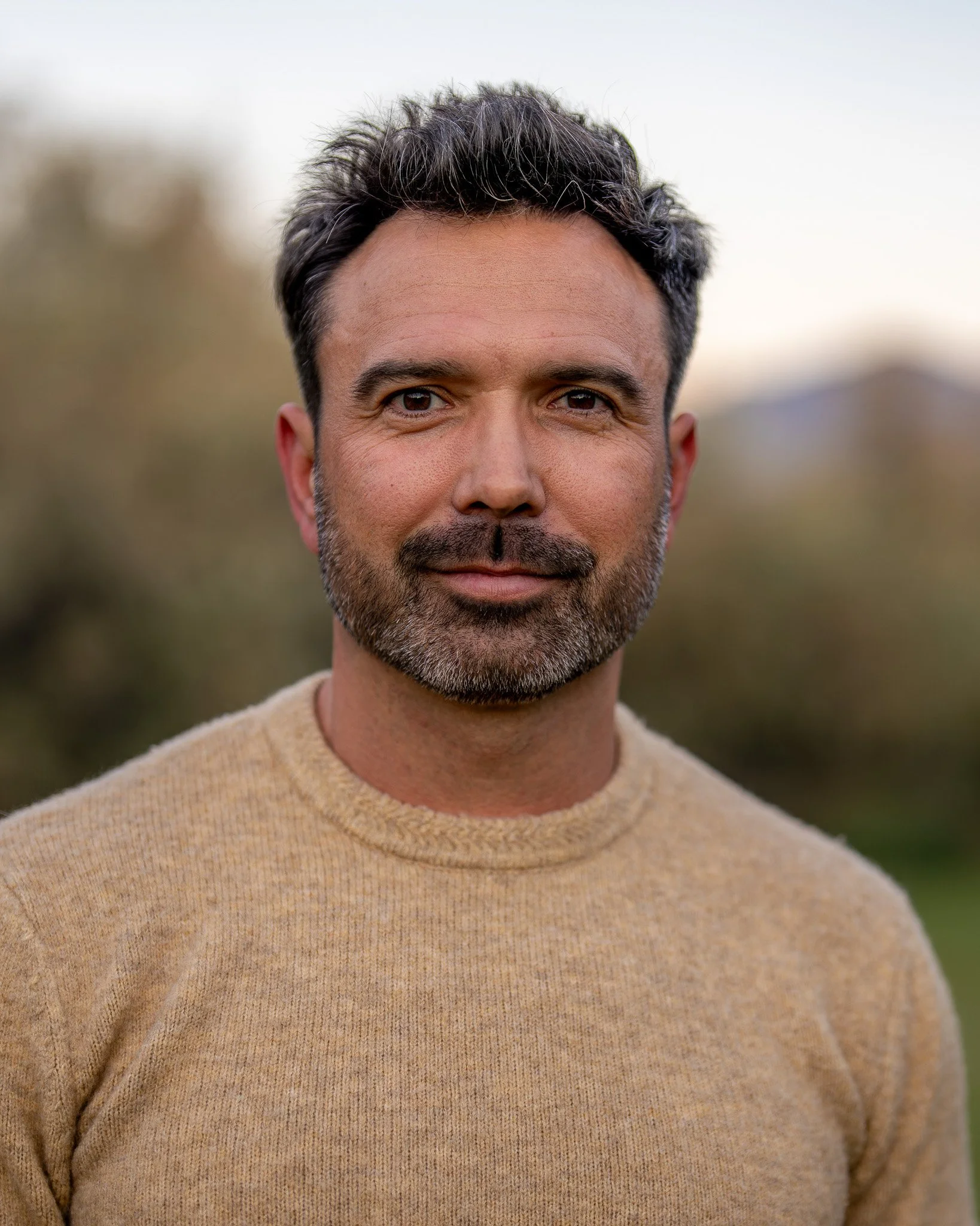 Man with short hair and beard wearing a beige sweater outdoors.