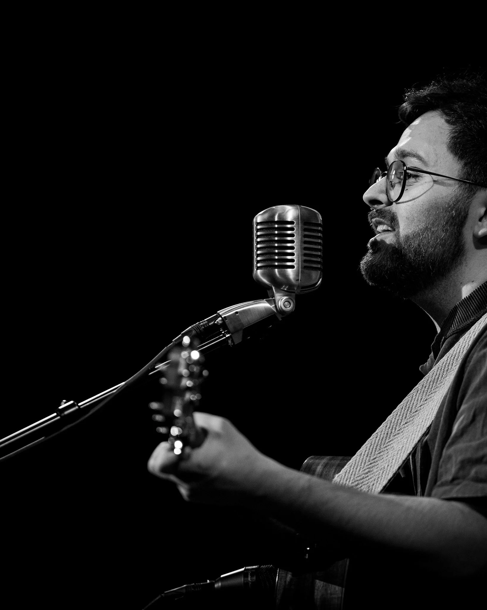 A black-and-white photo of a man singing and playing guitar into a vintage microphone.