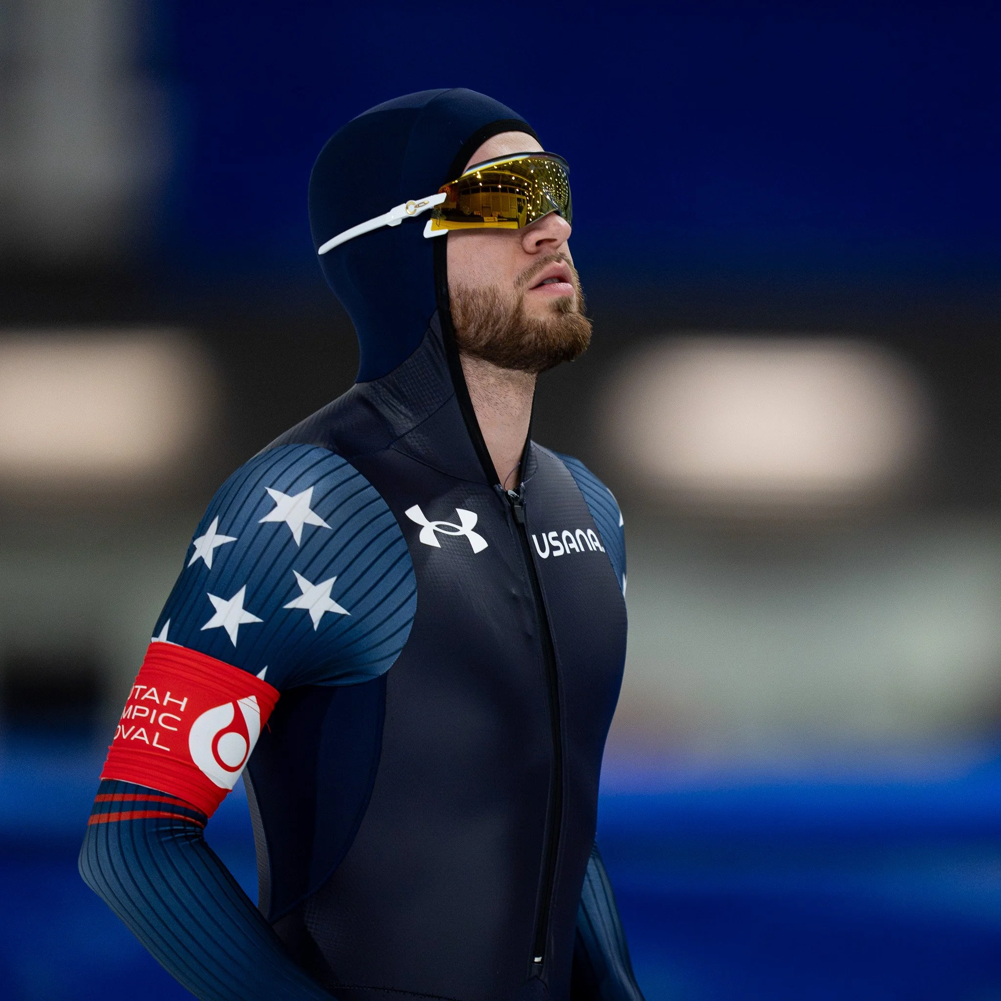 Speed skater in navy suit with star pattern, wearing protective goggles, during a competitive event.