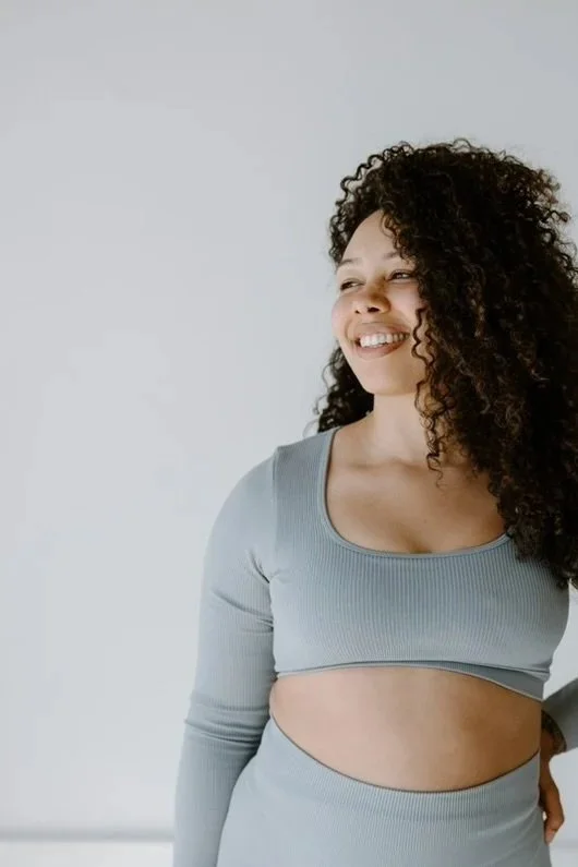 Woman with curly hair smiling, wearing a light gray long-sleeve crop top.