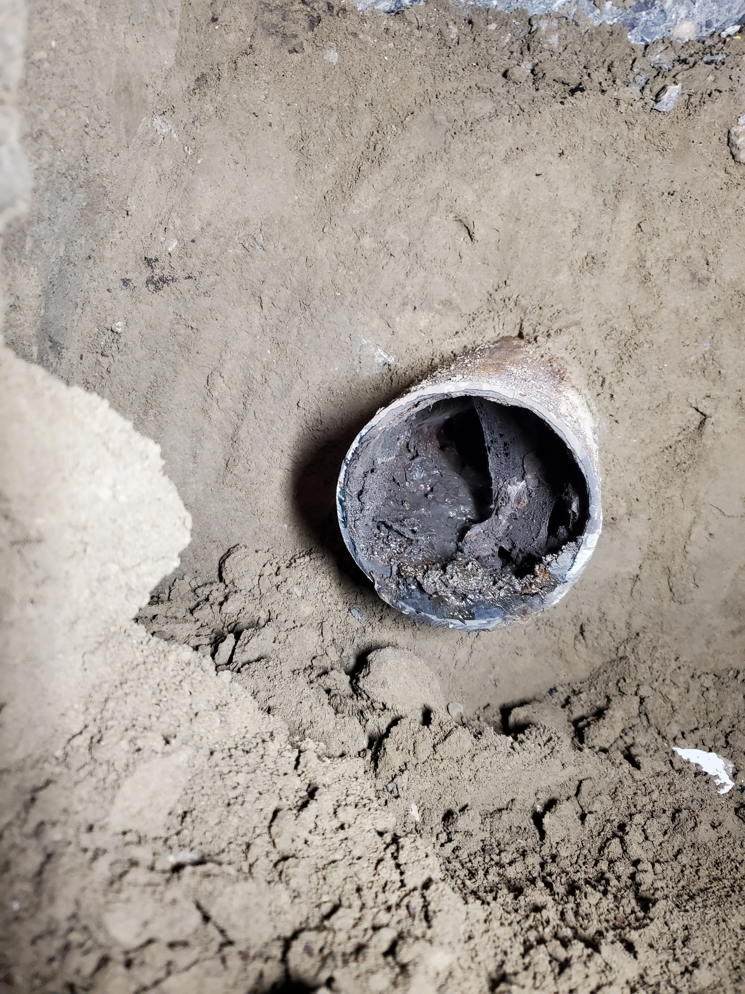 A close-up of a partially buried metal pipe in a sandy or dirt surface.