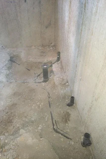 Bathroom plumbing pipes emerging from the floor and wall, in a construction or renovation setting.