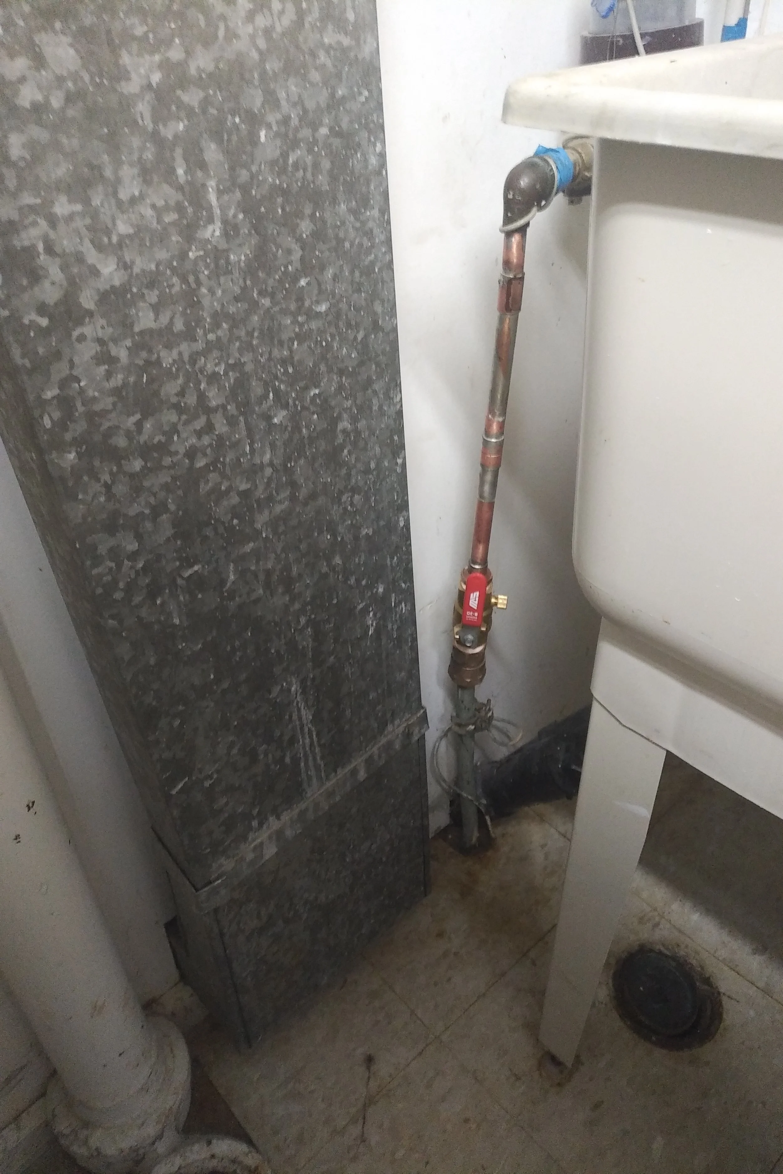 A close-up of a plumbing pipe with a shut-off valve next to a sink and a black cabinet in a utility room.