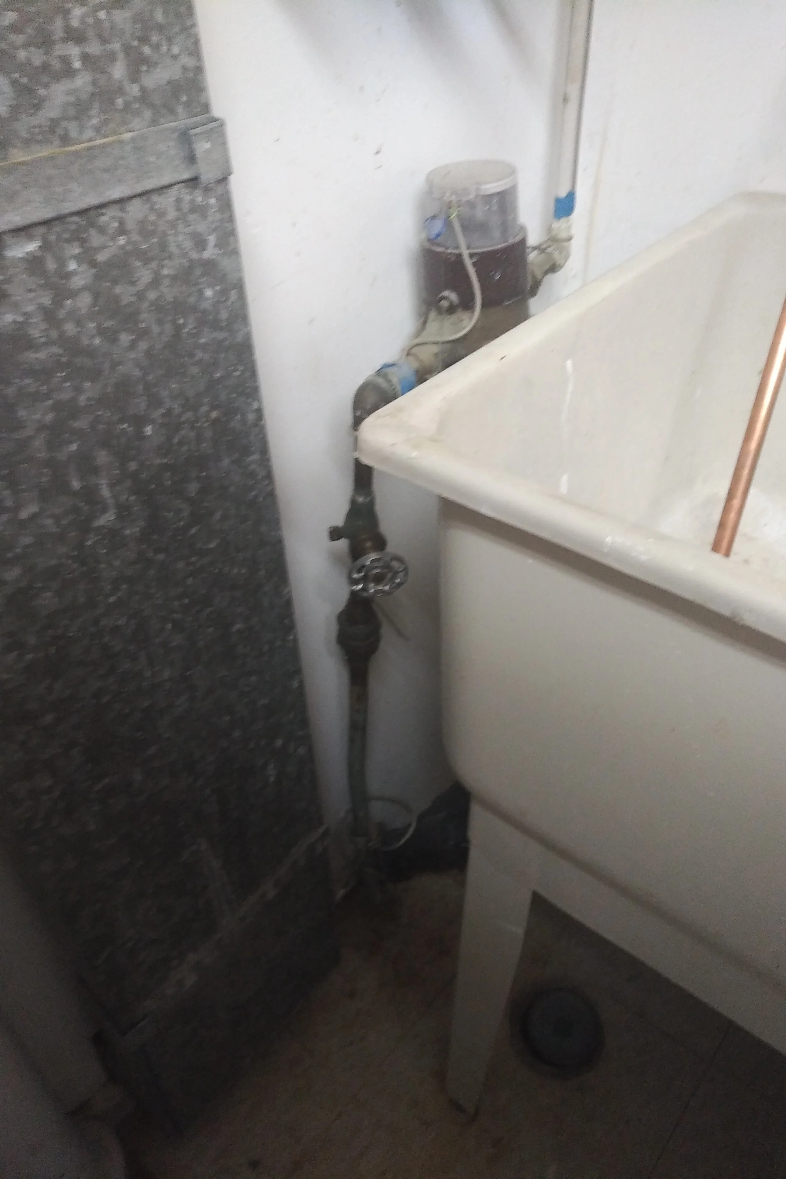 A utility sink with plumbing pipes and a water meter in a laundry or utility room.