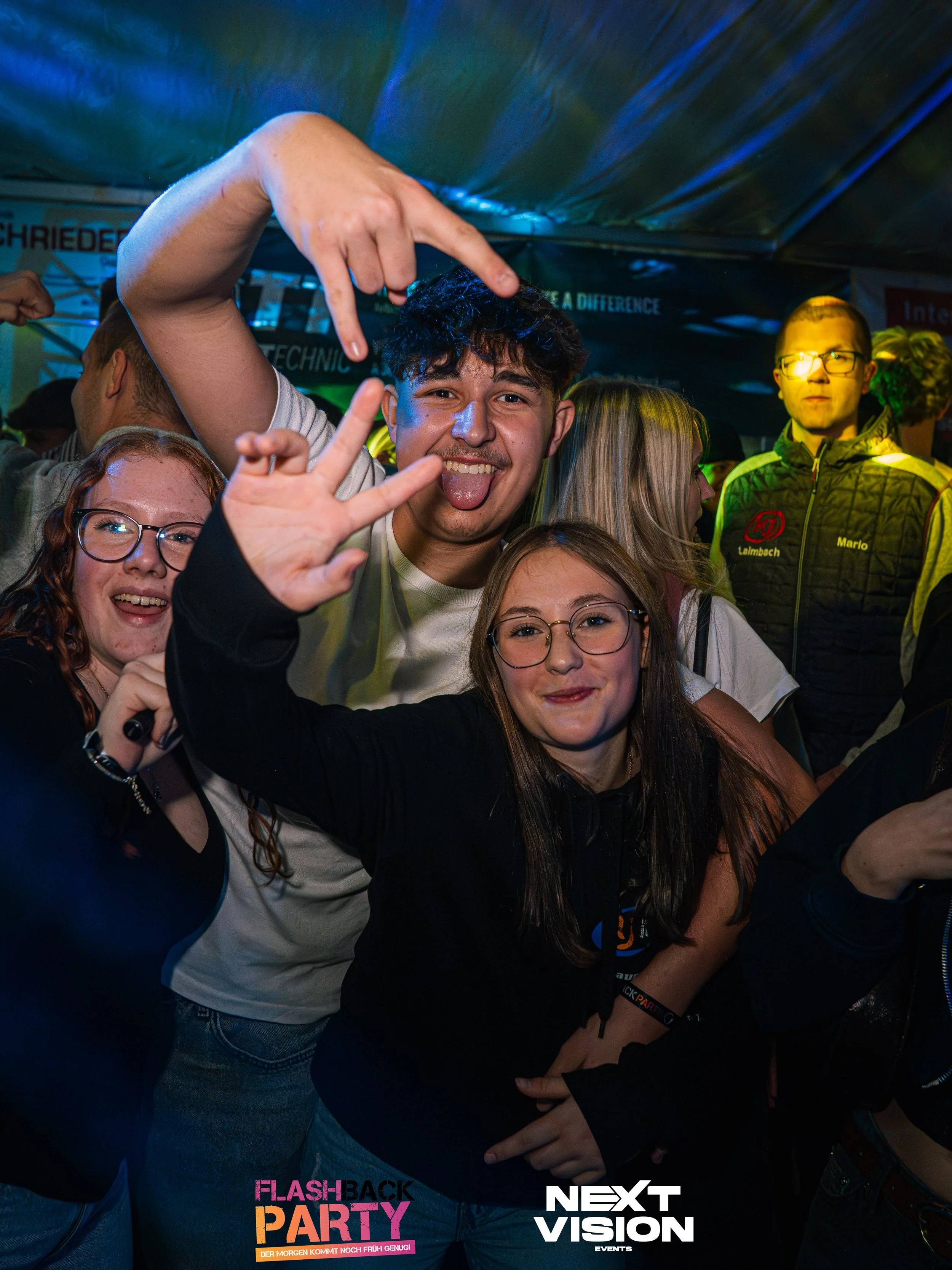 Gruppe junger Menschen, die auf einer Party feiern, dabei lachen und posieren.