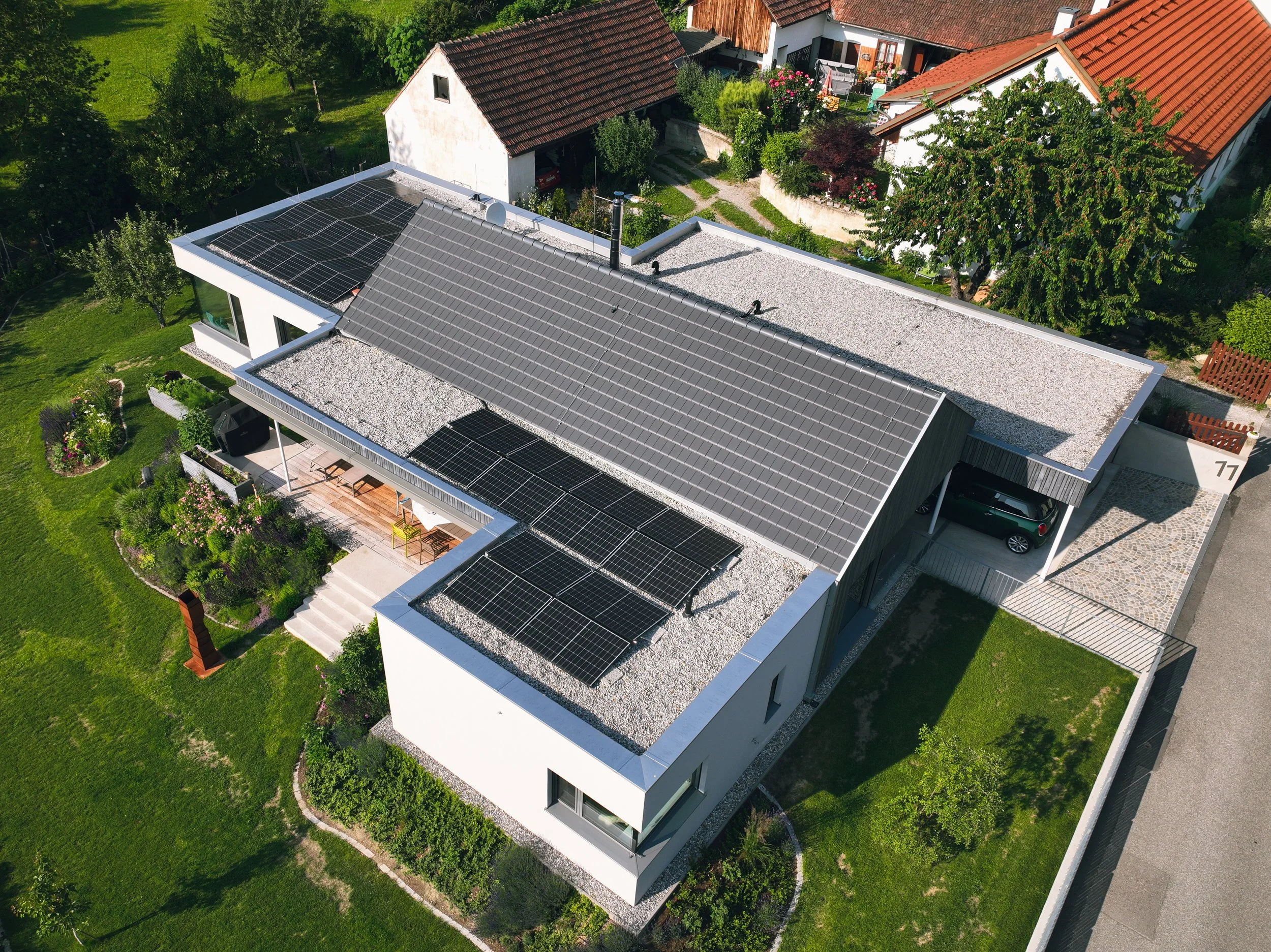Luftaufnahme eines modernen Hauses mit Solarpanelen auf dem Dach und einer gepflegten Gartenanlage.