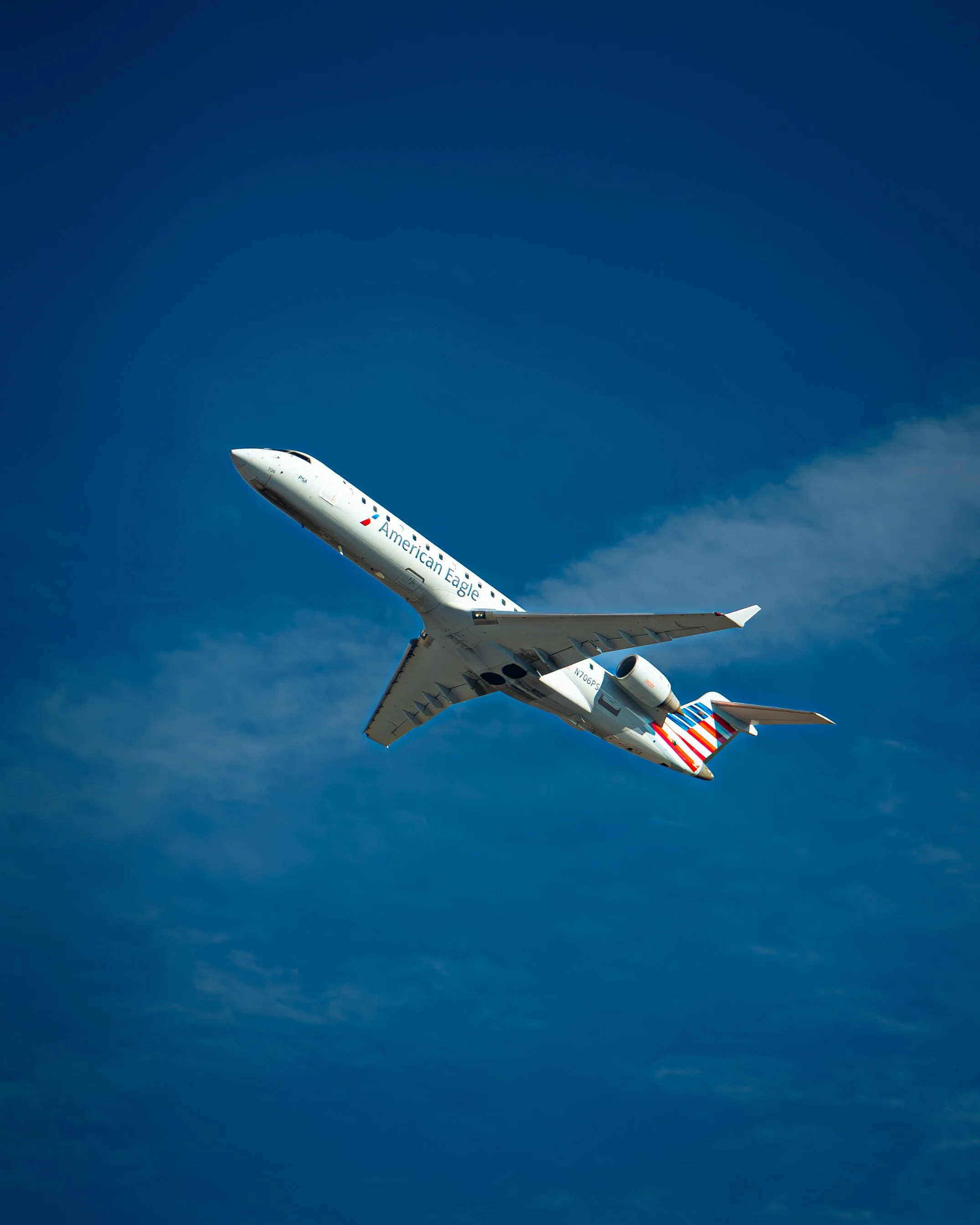Ein weißes Flugzeug mit amerikanischer Flagge am Heck fliegt gegen blauen Himmel.