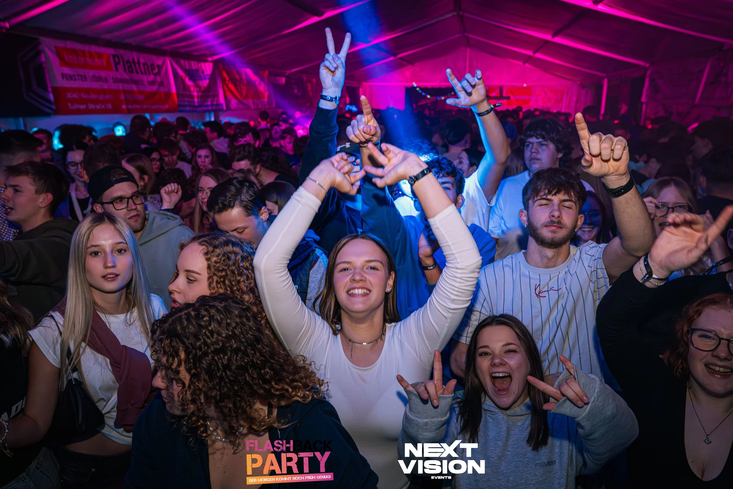 Menschen tanzen und feiern auf einer Partystimmung in einer mit buntem Licht beleuchteten Veranstaltungshalle.