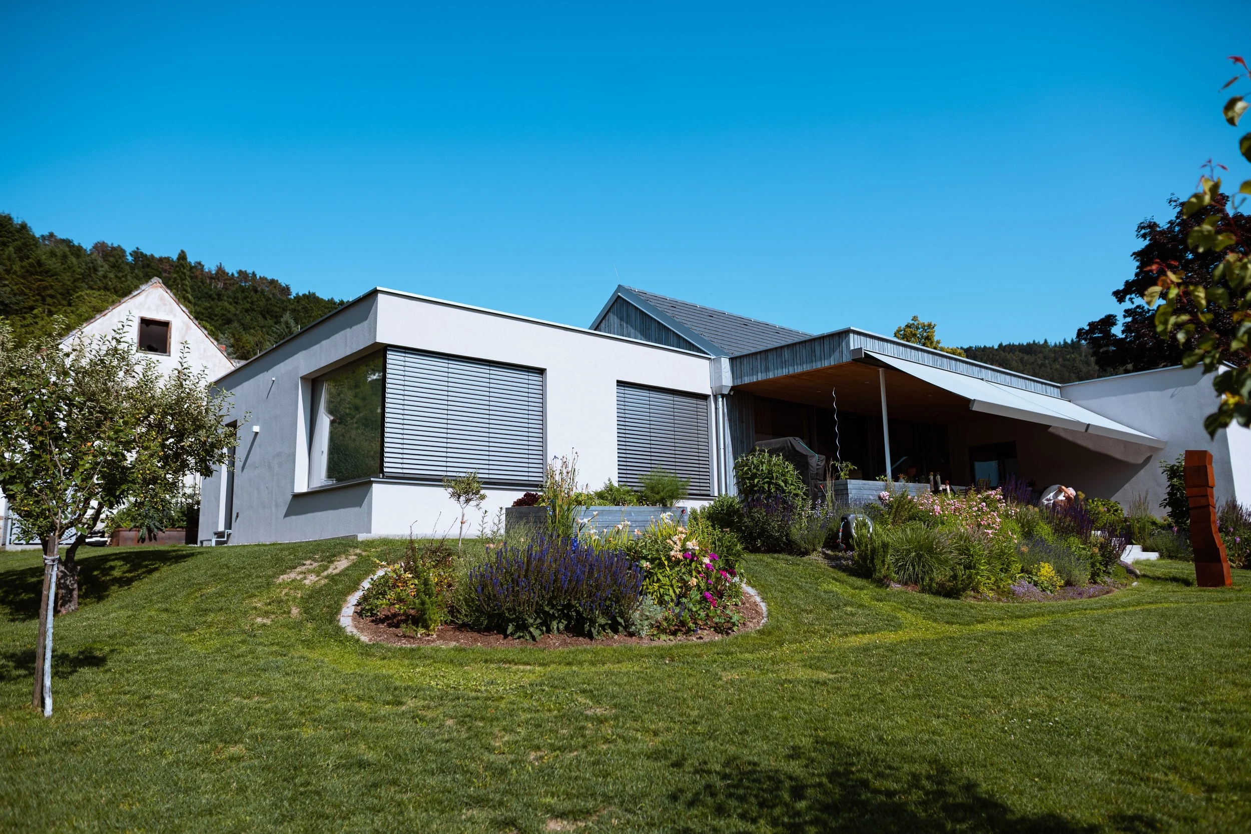 Moderner Einfamilienhaus mit Garten, blauer Himmel und grünem Rasen.