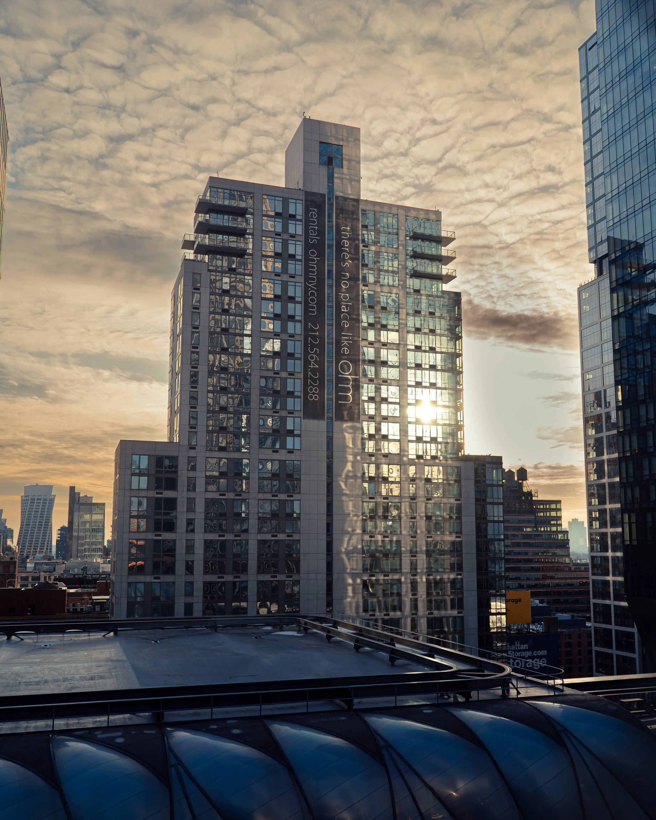 Hochhäuser in einer Stadt bei Sonnenuntergang mit bewölktem Himmel, reflektierende Fassaden und eine Anzeigetafel an einem Gebäude