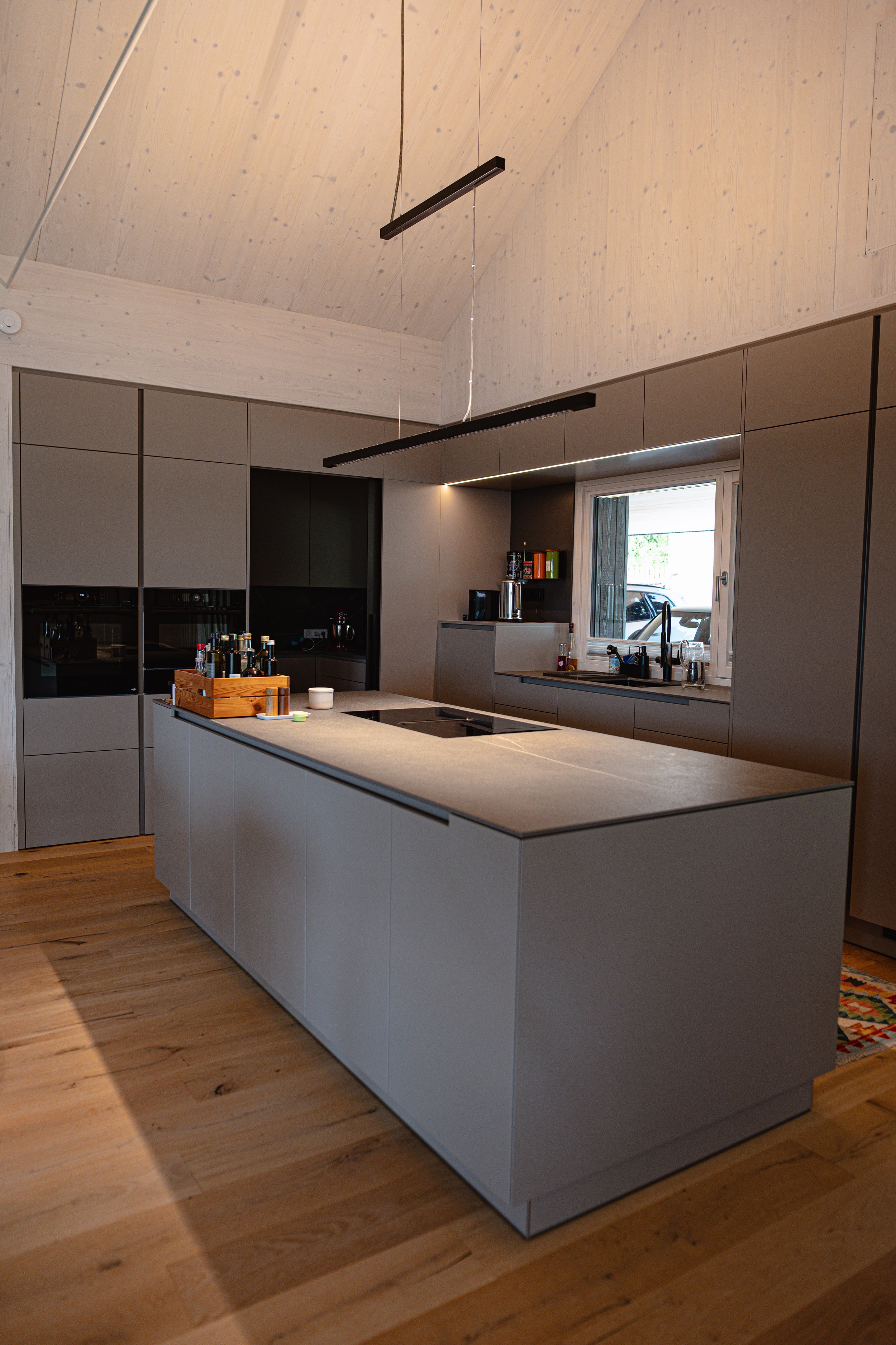 Moderne Küche mit grauen Schränken, Holzfußboden und einem Küchenblock in der Mitte