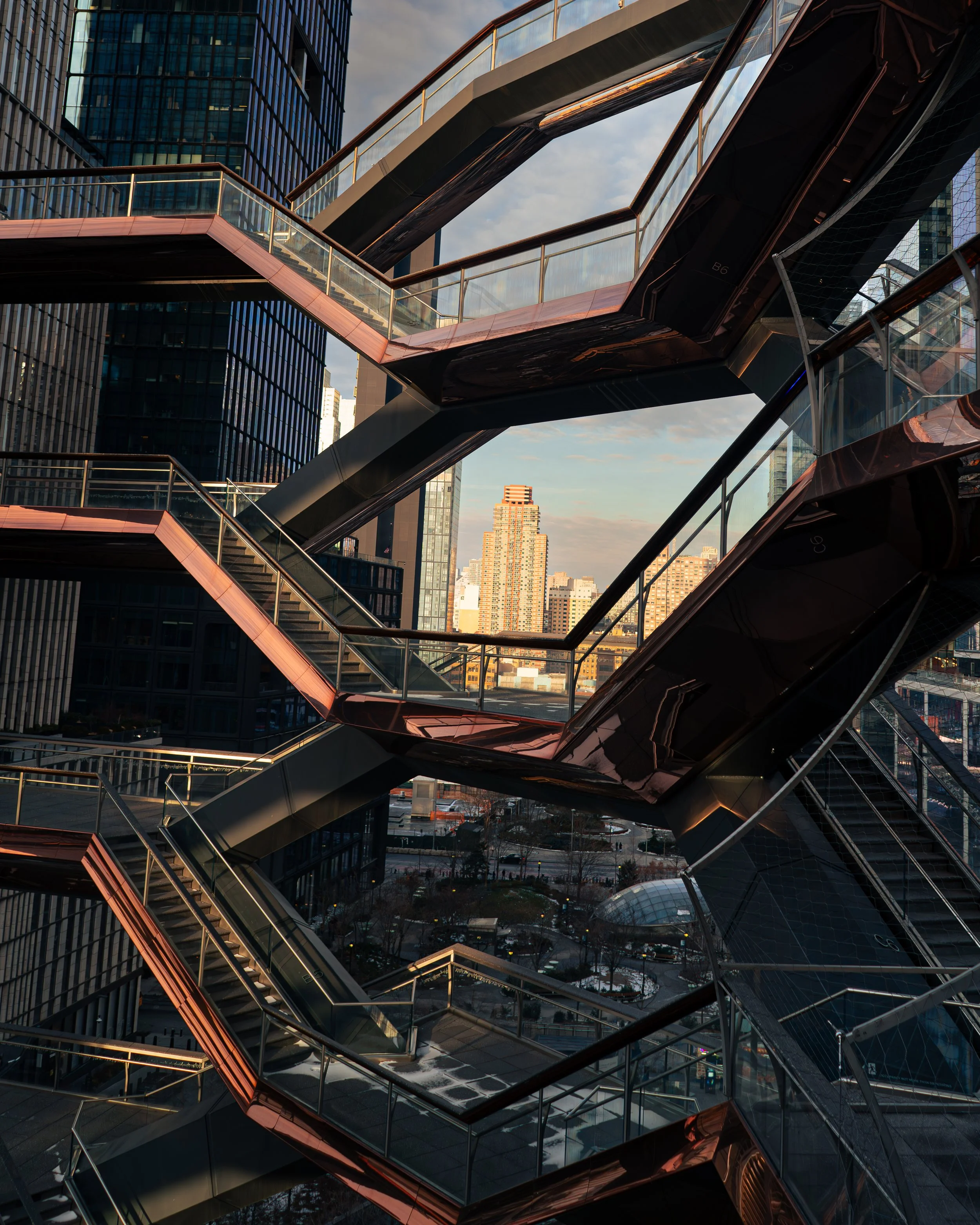 Moderne Gebäudefassade mit spiegelnden Oberflächen und mehrstöckigen Skywalks in einer Stadt bei Sonnenuntergang.