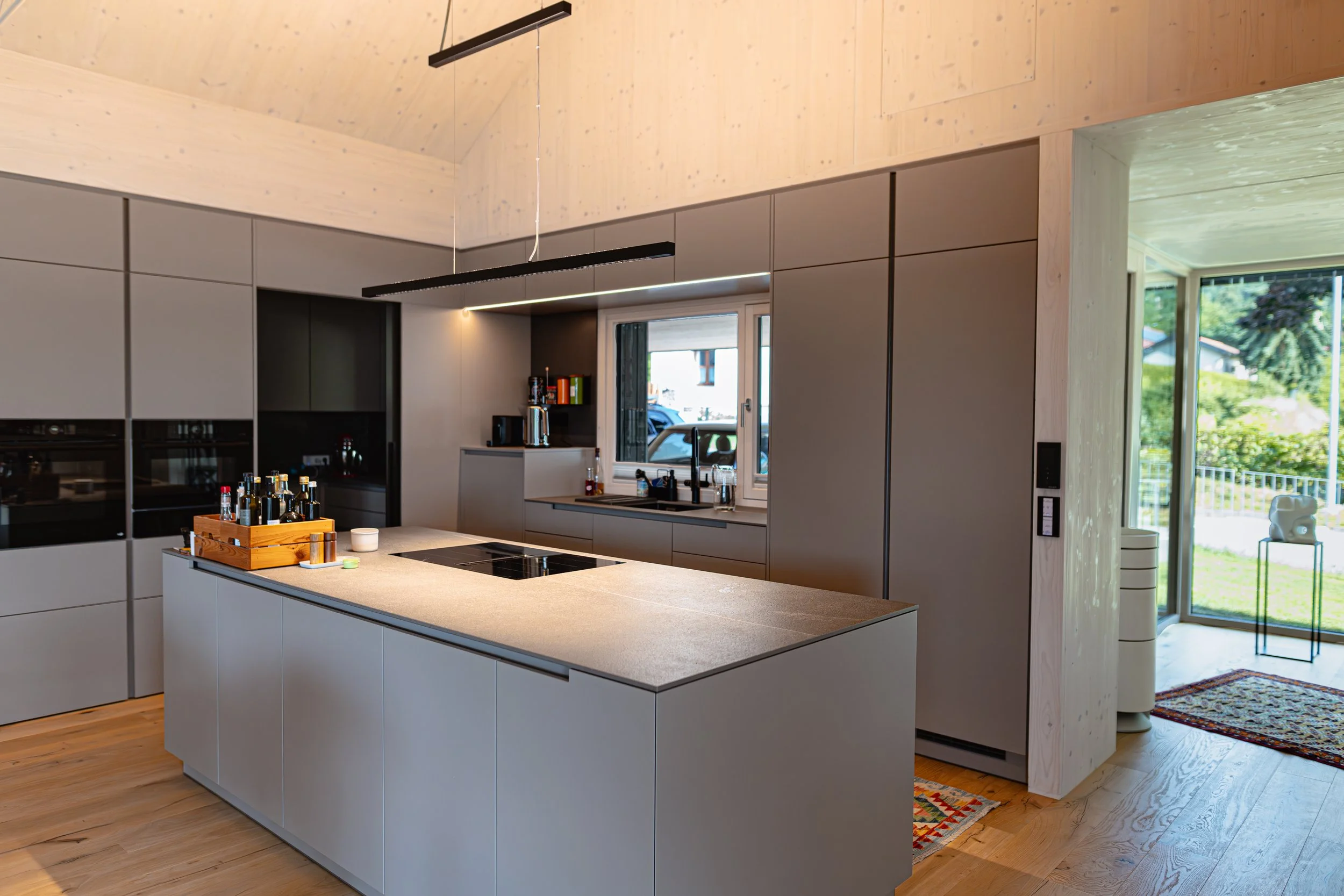 Moderne, minimalistische Küche mit grauen Schränken, Kücheninsel und Holzboden, große Fenster mit Blick nach draußen