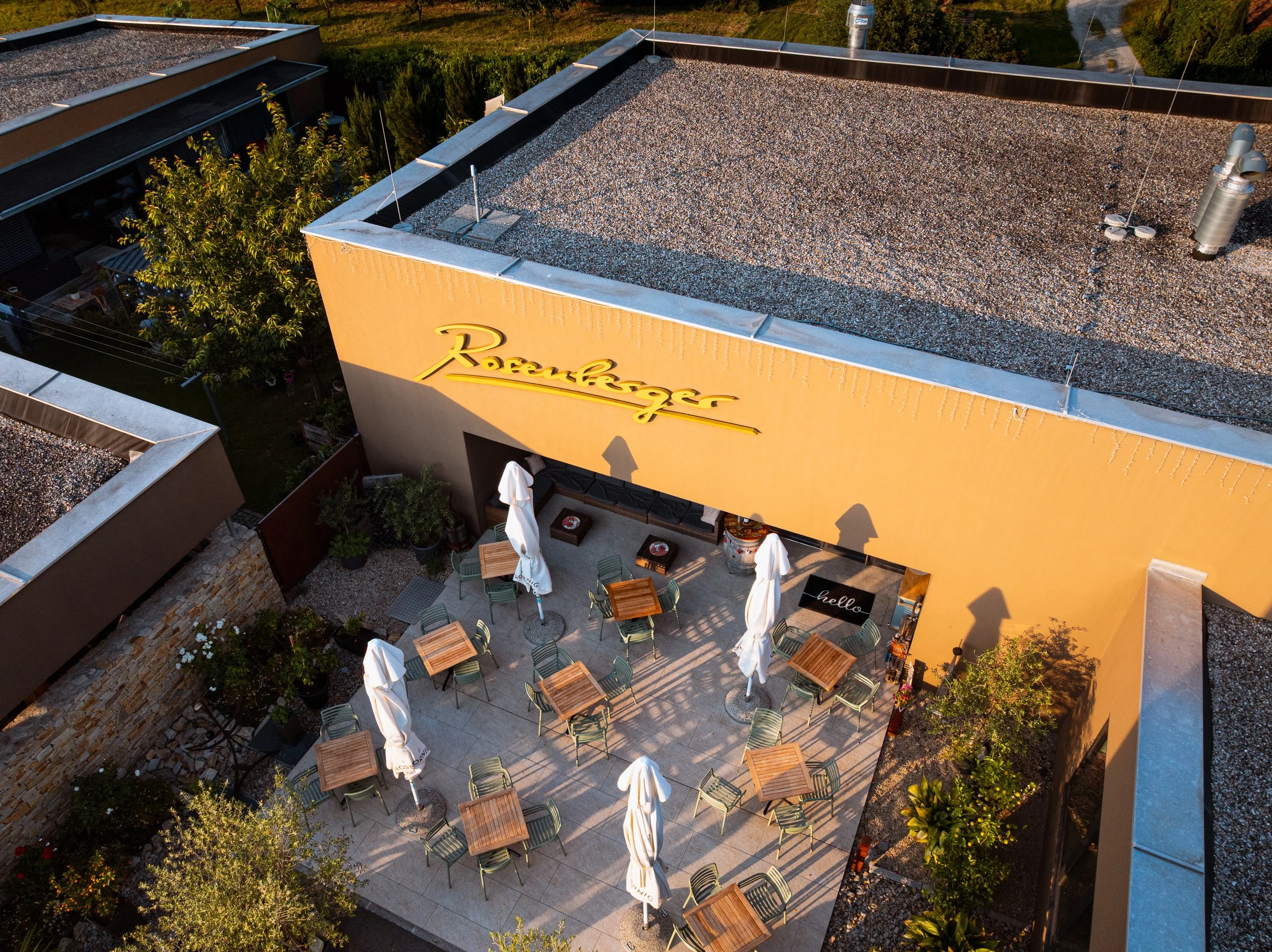 Vogelperspektive auf eine Terrasse mit Tischen, Stühlen und Sonnenschirmen vor einem gelben Gebäude mit dem Schriftzug "Rosenkeller".