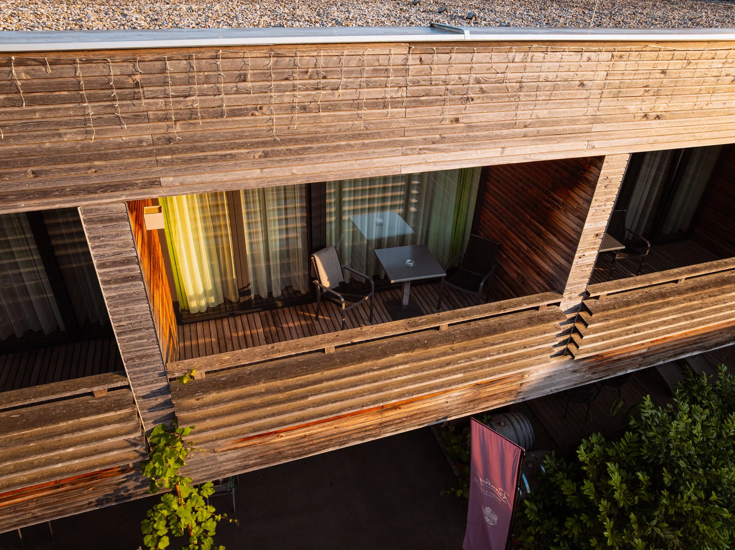 Blick auf einen Balkon eines Holzgebäudes mit Stühlen, Tischen, Vorhängen und einigen Pflanzen.