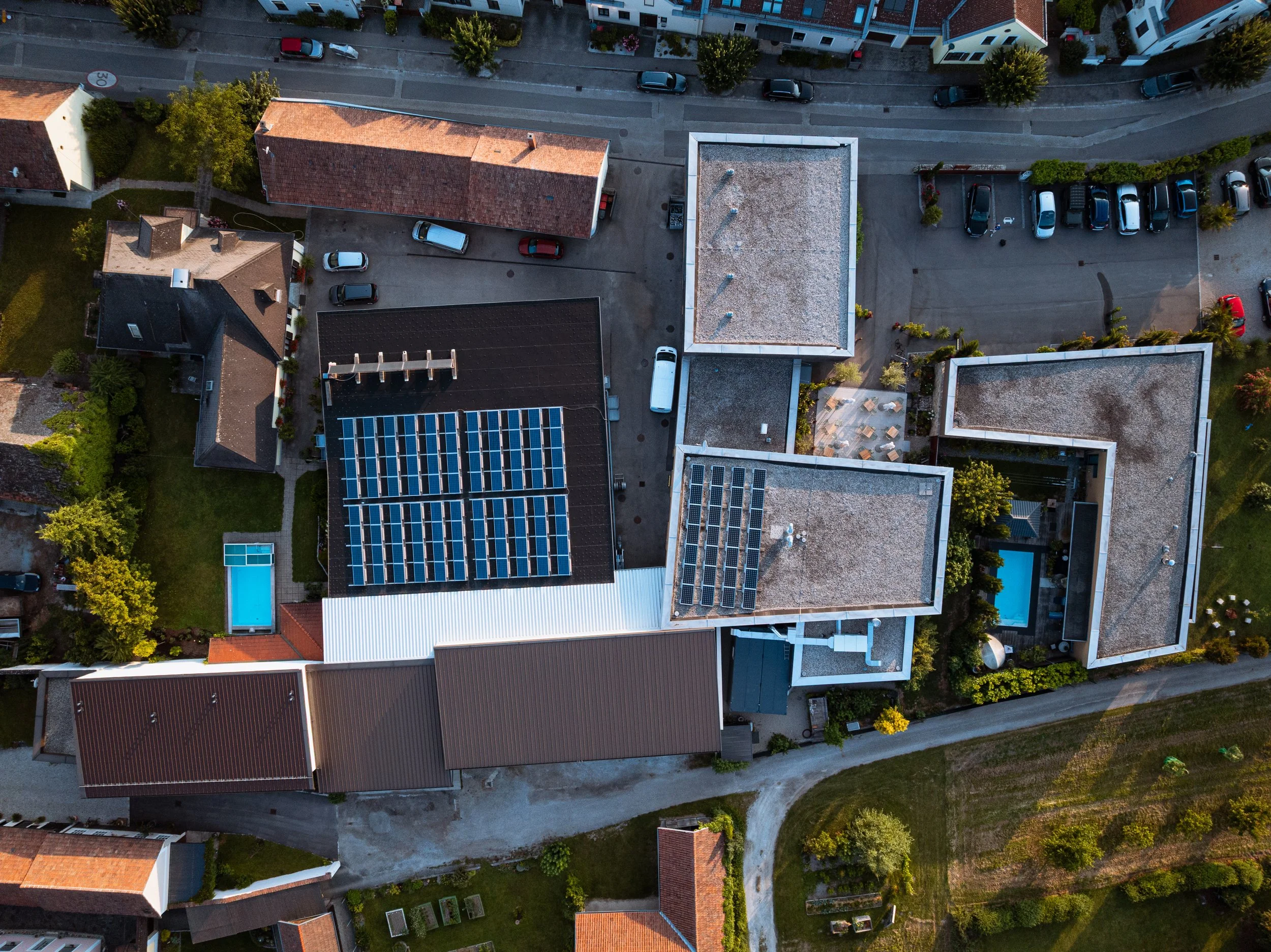 Vogelperspektive auf mehrere Gebäude mit Solarpanelen und Swimmingpool, umgeben von Bäumen und Straßen in einer Wohngegend.