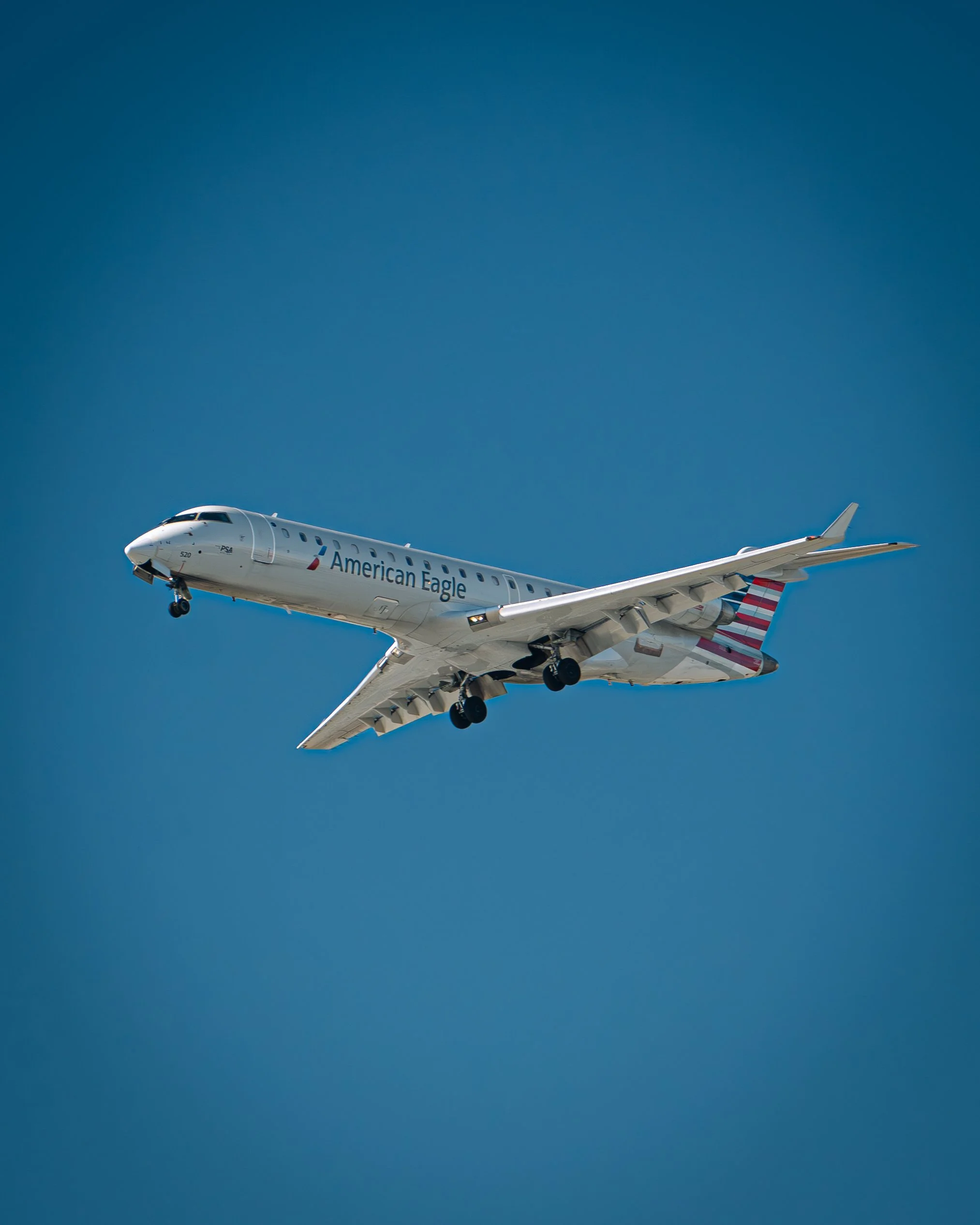 Ein weißes Flugzeug mit 'American Eagle'-Logo fliegt am blauen Himmel.