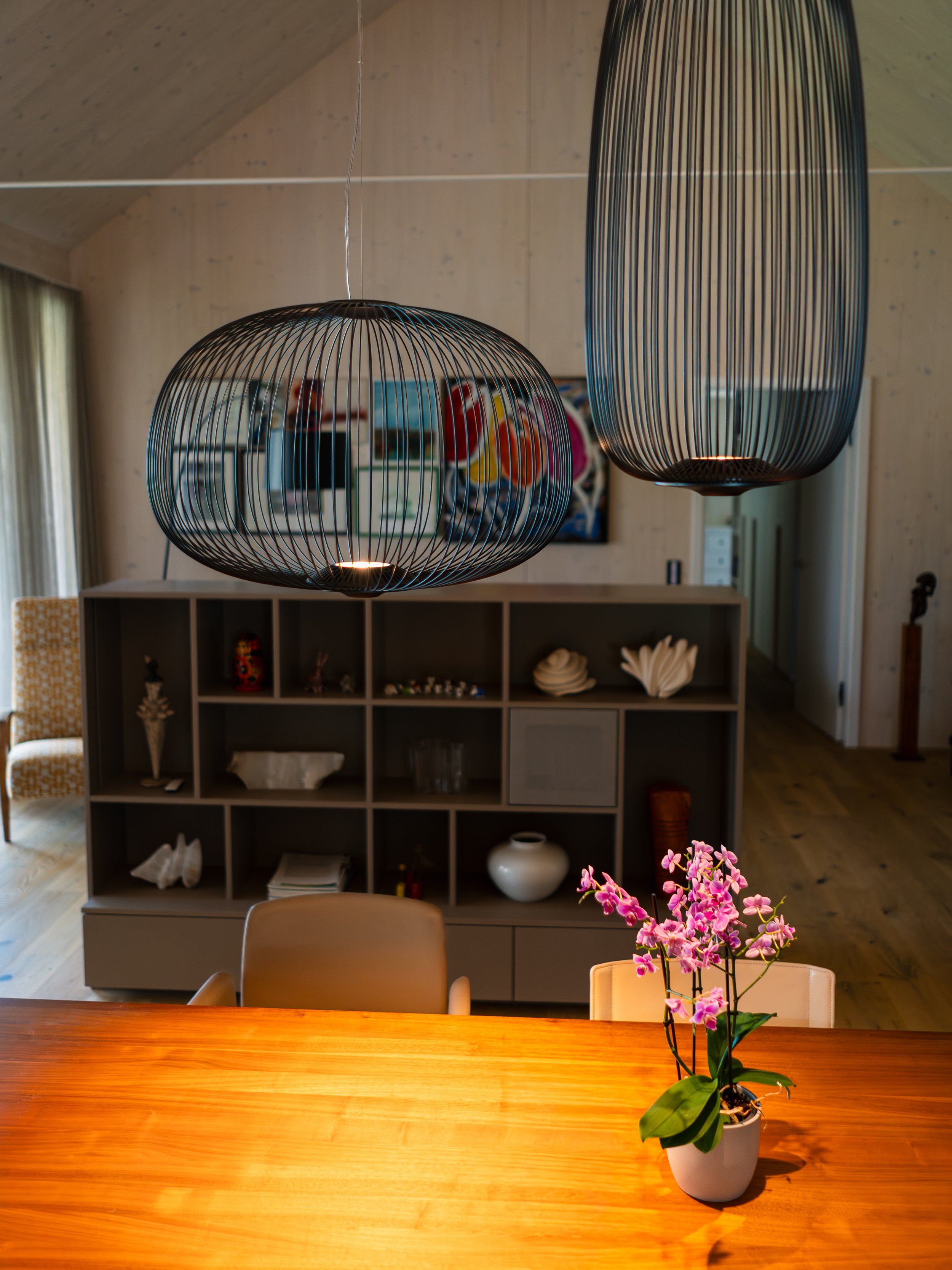 Ein Esszimmertisch mit einer weißen Orchideenpflanze in einer weißen Vase, darüber hängen zwei moderne, schwarze Hängeleuchten.