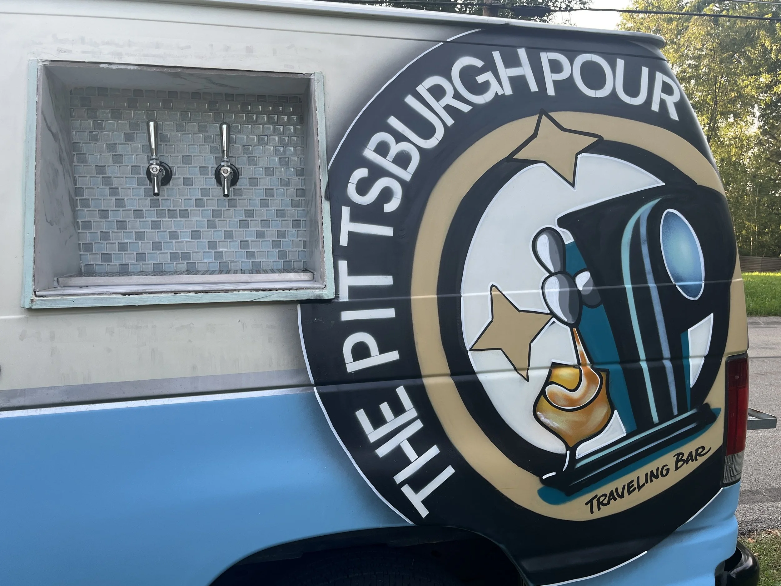 A food truck with a large circular logo featuring a cartoon of a spaceship with stars and the text 'THE PISTBURGH POUT' and 'TRAVELING BAR'.