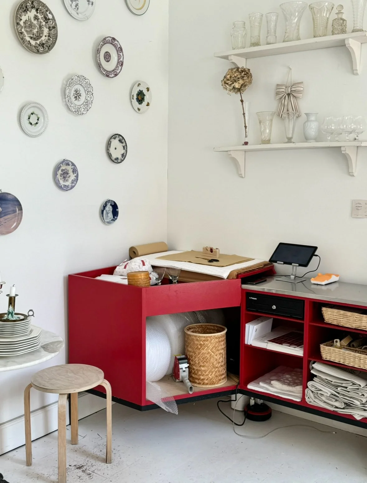Interior at Joliment Vintage, showing a red worktable and white walls decorated with porcelain plates.
