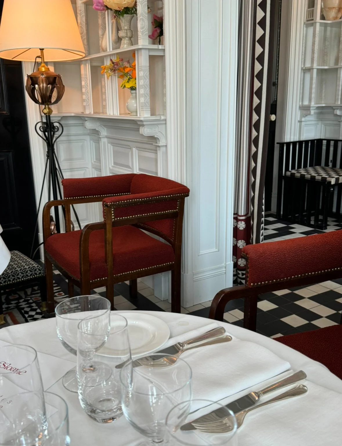 A snapshot of the Dining Room, with black and white tiles, red velvet chairs, silver utensils on white linen.