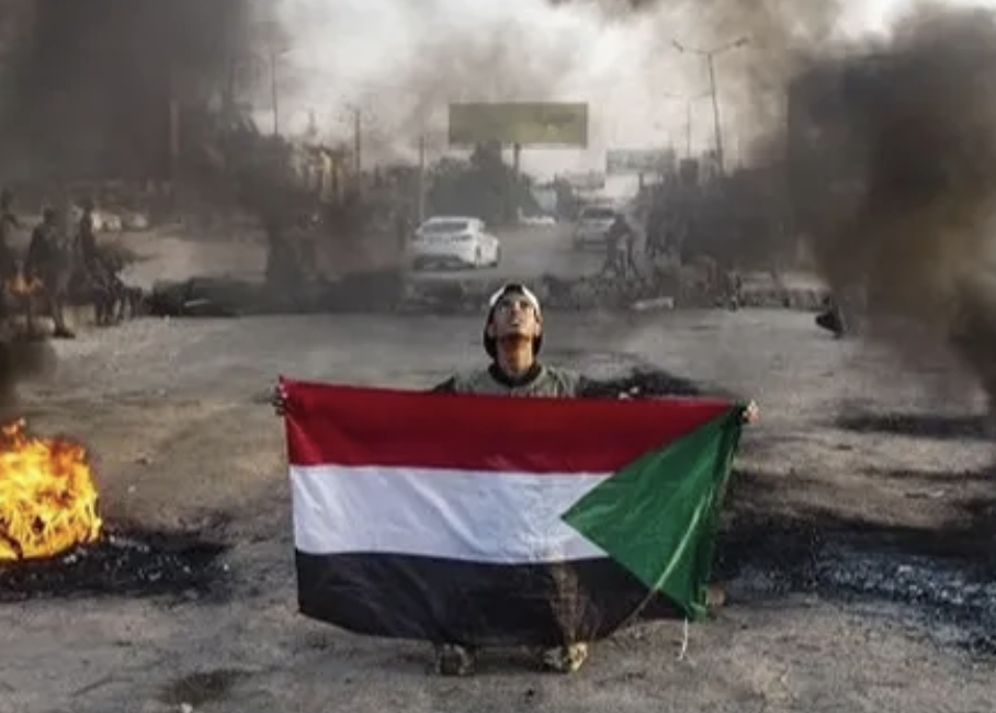 picture of a Sudanese flag being held up on a burnt landscape