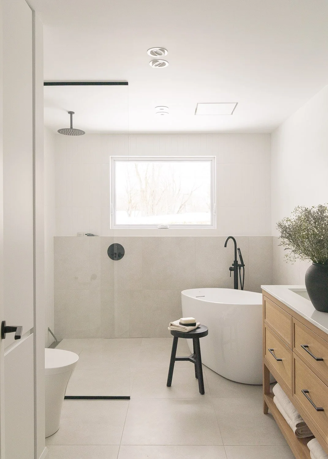 Salle de bain moderne et lumineuse de la Résidence ARST conçue par Ateliers Royer, avec vanity en bois sur mesure, baignoire autoportante, douche à l'italienne et robinetterie noire mate.