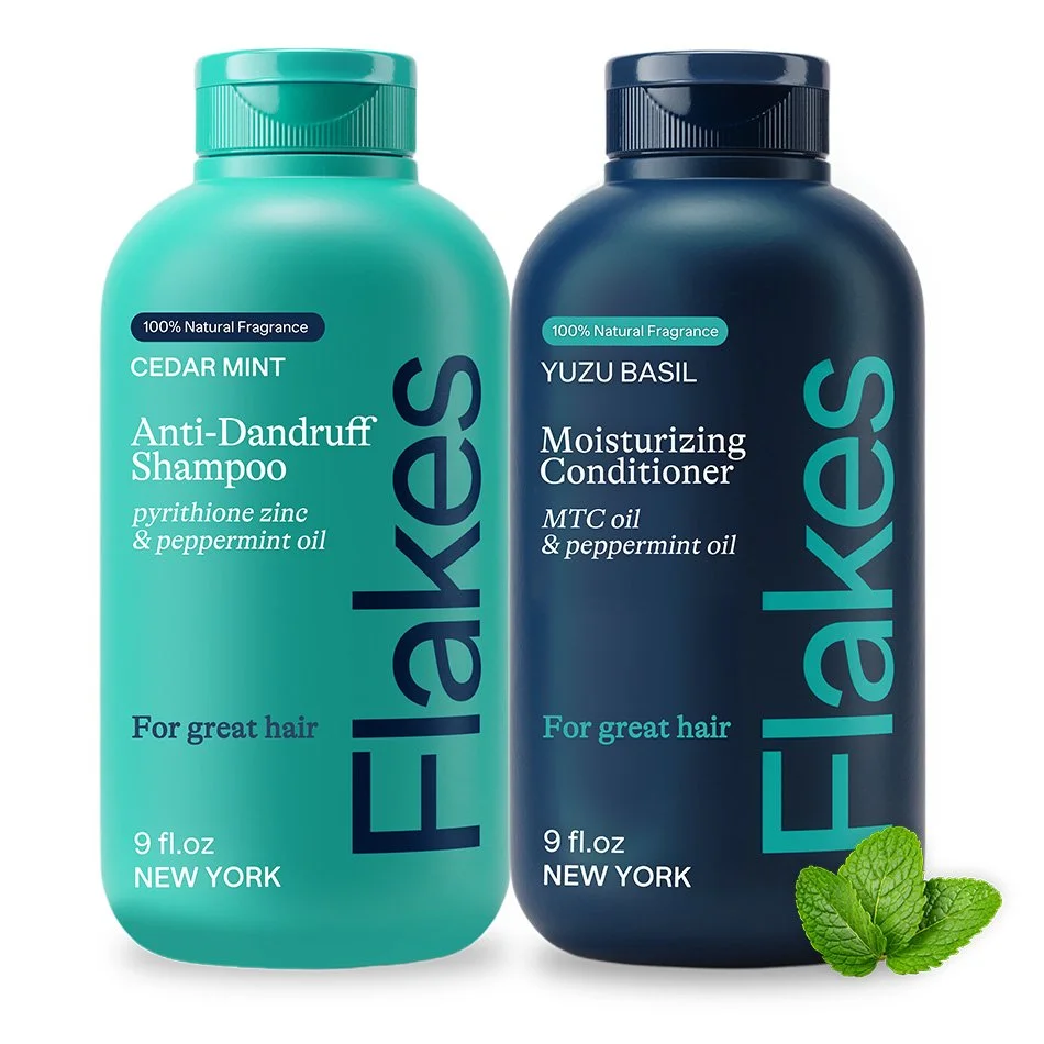 Two bottles of hair products: one teal anti-dandruff shampoo with cedar mint, and one navy moisturizing conditioner with yuzu basil, both featuring peppermint oil and natural fragrance.