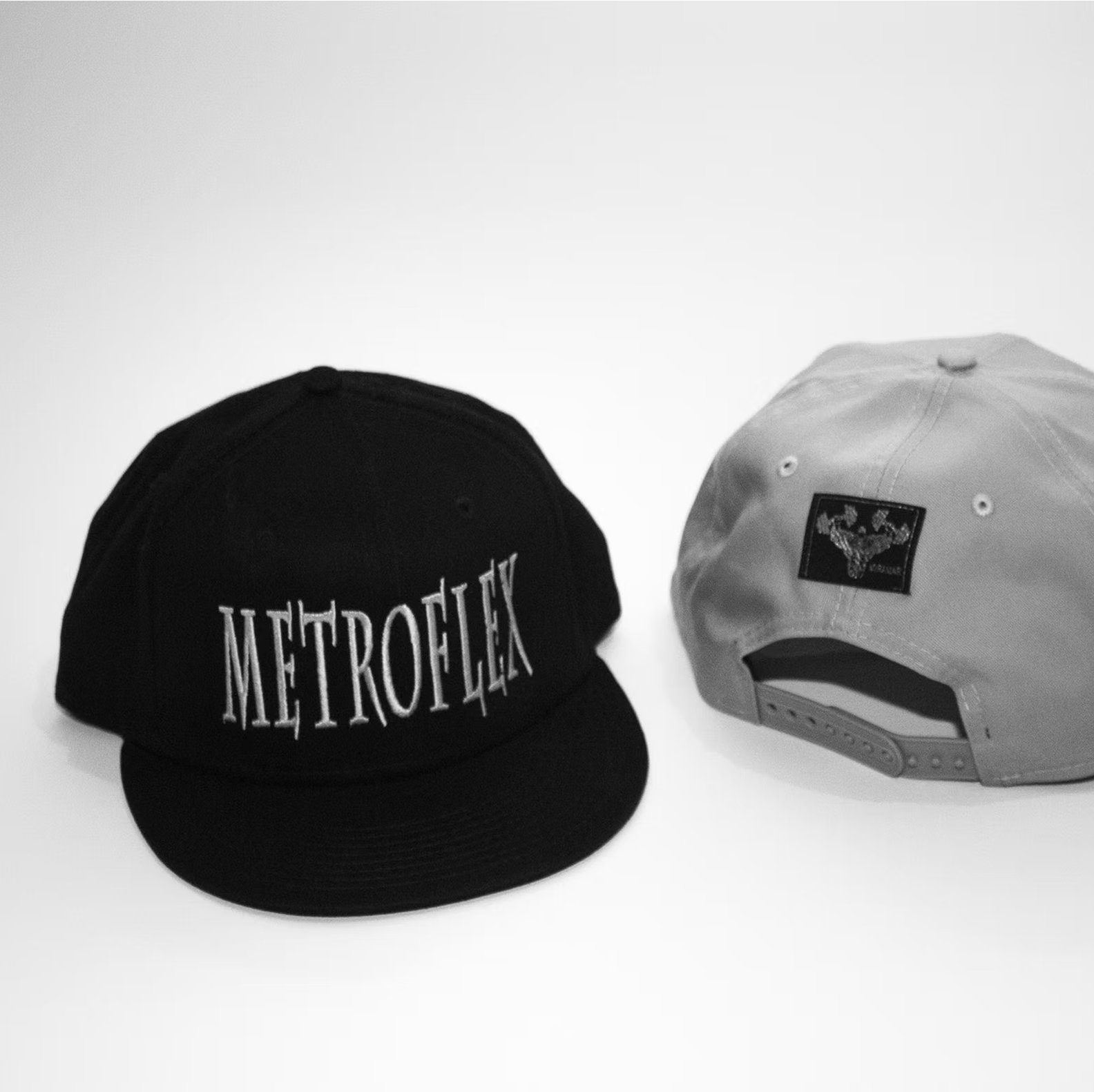 Two snapback hats, one black with "METROFLEX" text and one gray with a logo tag, displayed on a plain background.