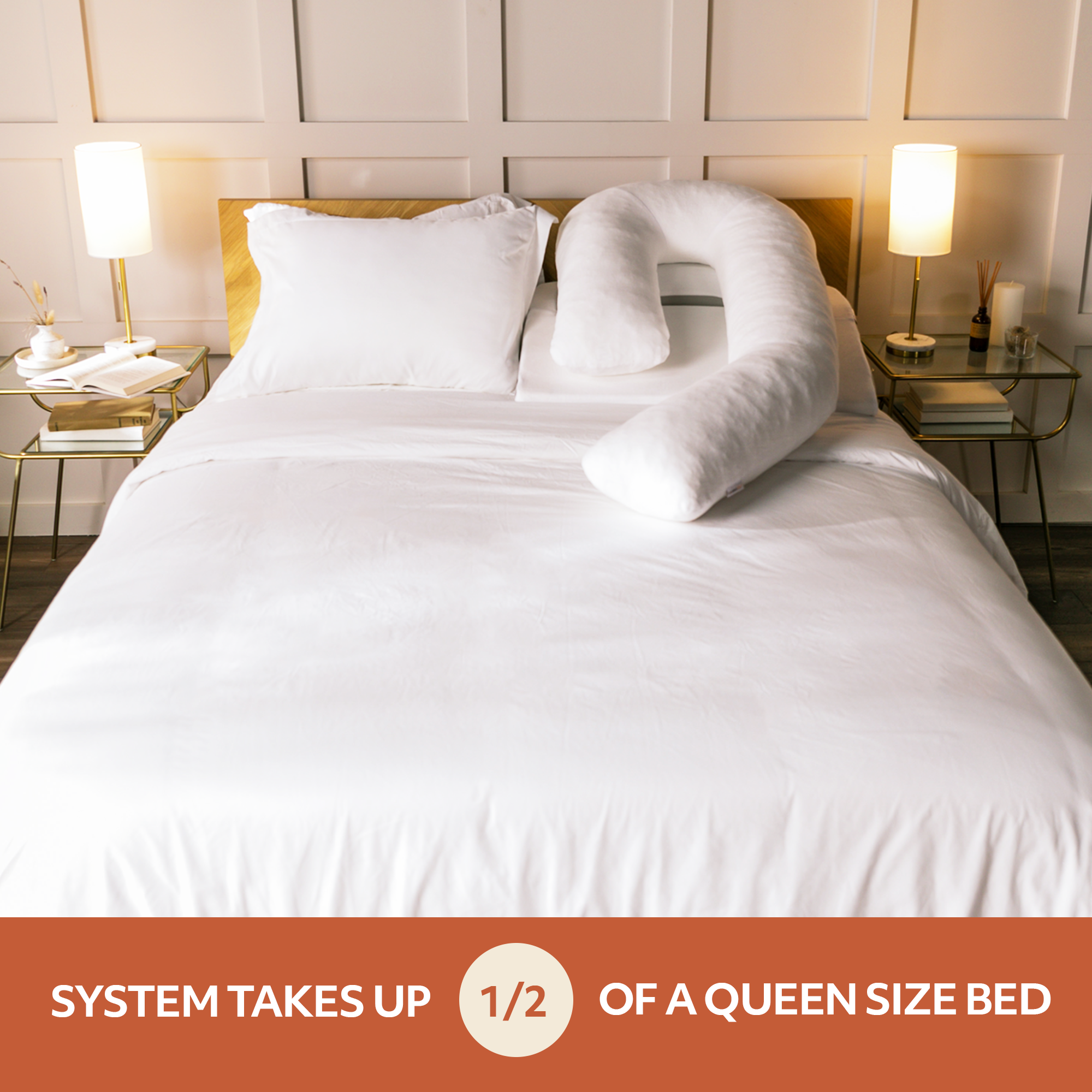 A queen-sized bed with white sheets and pillows featuring a U-shaped body pillow. Two nightstands with lamps and decor items are on each side. Text indicates the setup takes up half of the bed.