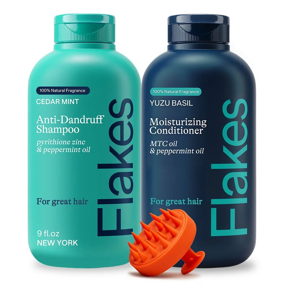 Two bottles of hair care products labeled "Flakes" with a scalp massager. The first bottle is Cedar Mint Anti-Dandruff Shampoo containing pyrithione zinc and peppermint oil. The second is Yuzu Basil Moisturizing Conditioner containing MTC oil and peppermint oil. Both feature 100% natural fragrance.