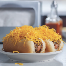 Two chili cheese dogs with shredded cheddar on a plate
