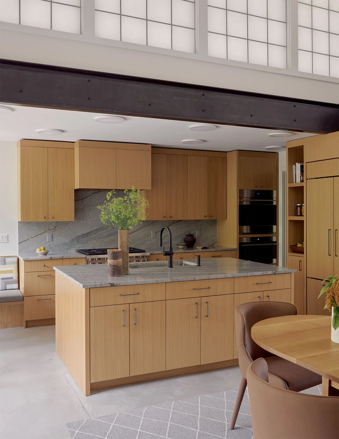 Modern kitchen with wooden cabinets, marble island, and built-in appliances in an open-concept space.