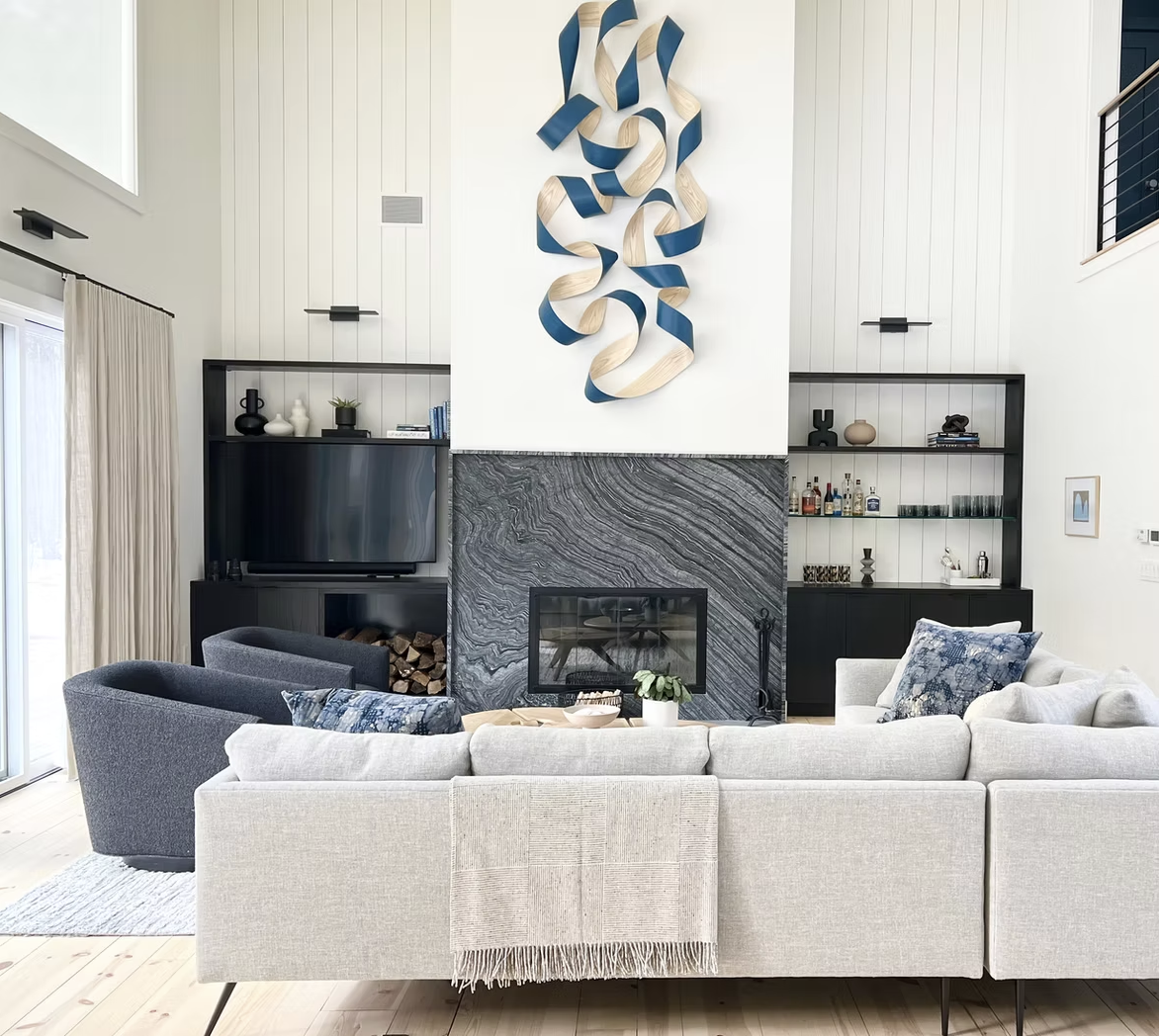 Modern living room with white sofa, black fireplace with marble surround, wall-mounted TV, and heron-shaped wall art.