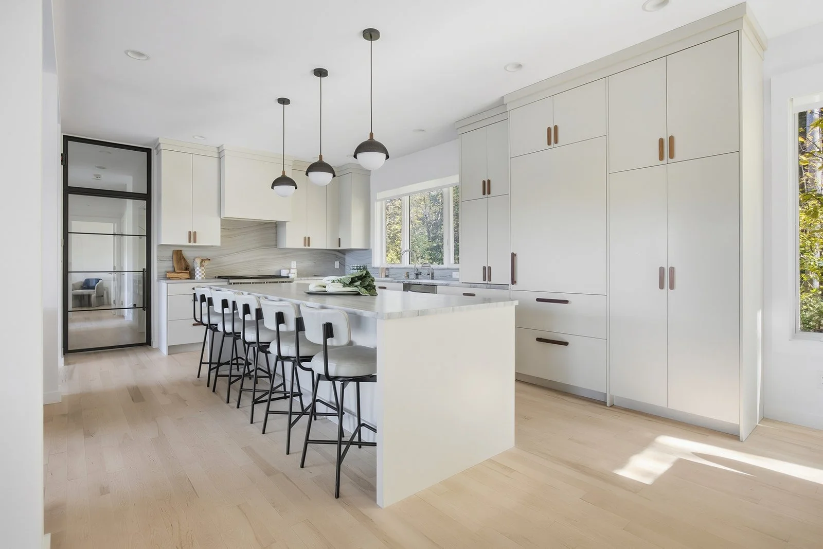 Modern kitchen with white cabinets, a large island with barstools, pendant lighting, large windows, and a sliding glass door.