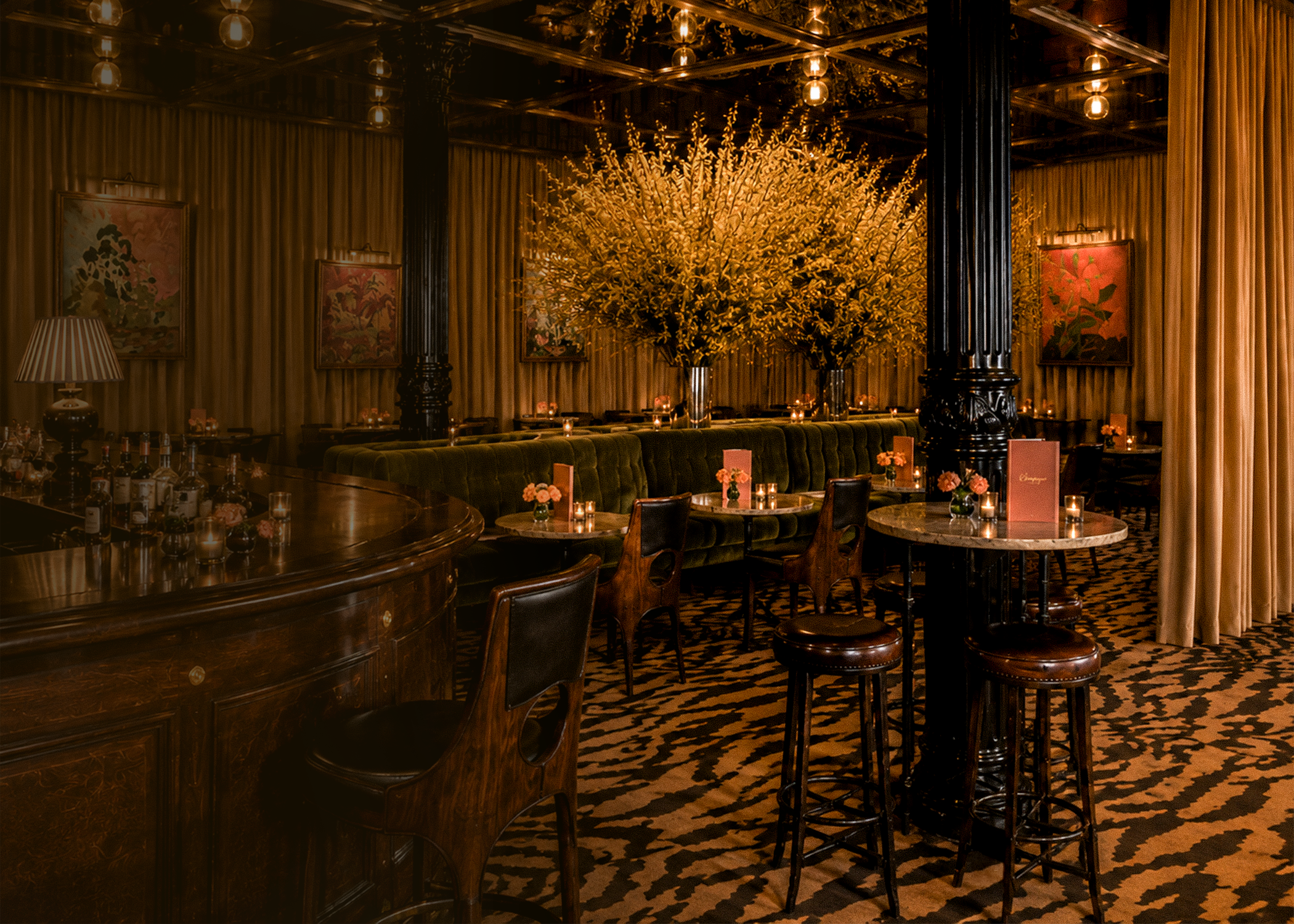 Elegant restaurant interior with large floral arrangement, wooden bar, velvet seating, and framed artwork with botanical theme, dim lighting.