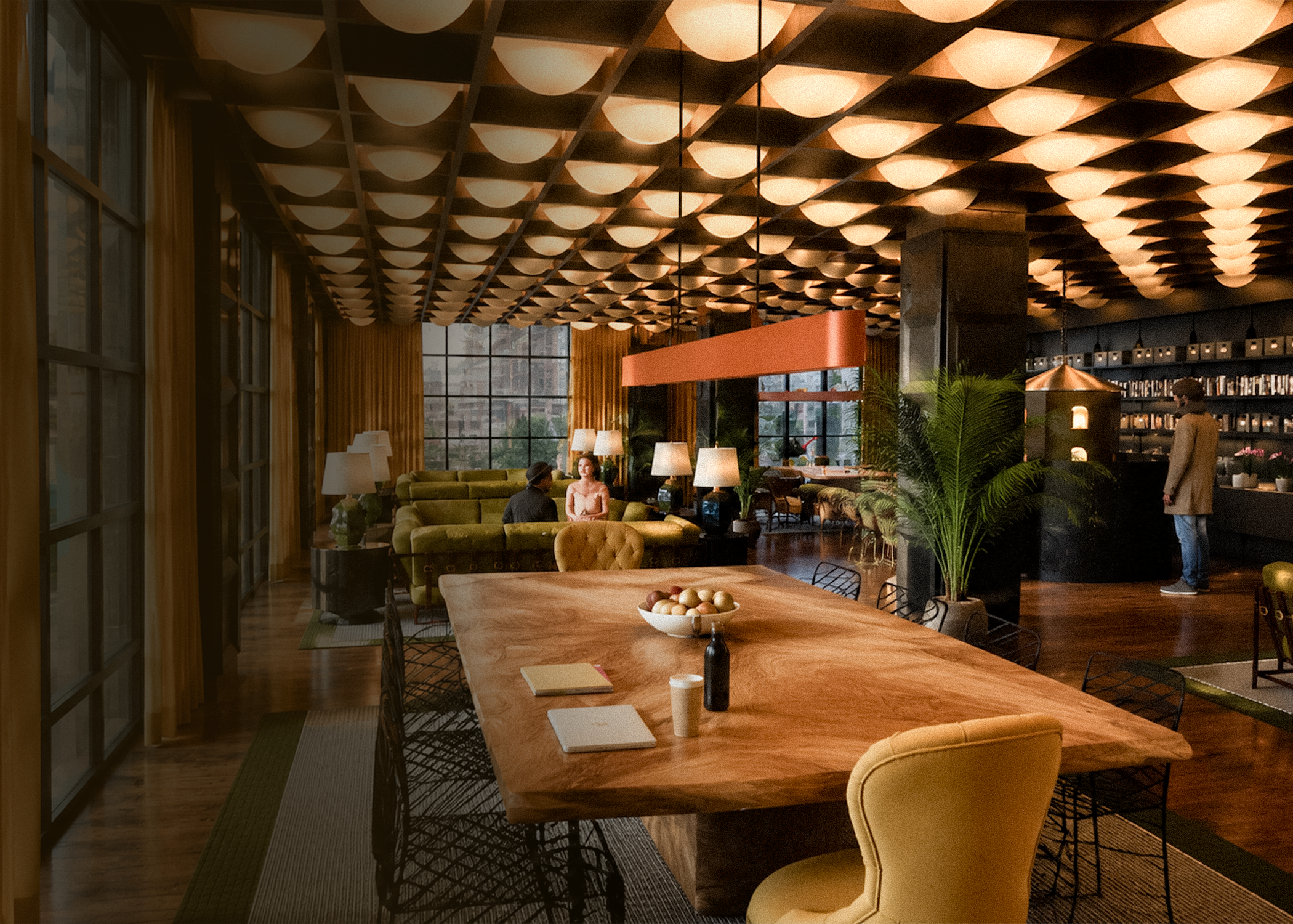 A modern, warmly lit interior lounge with a large wooden dining table in the foreground, yellow armchairs, green sofas, several standing lamps, large windows with yellow curtains, and a ceiling with geometric patterned lighting fixtures.