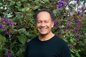 A smiling man standing in front of purple flowering plants.
