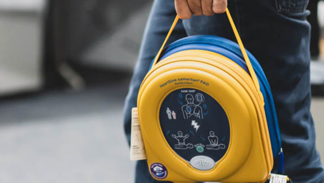 A person holding a yellow AED training pad case with medical instructions printed on it.