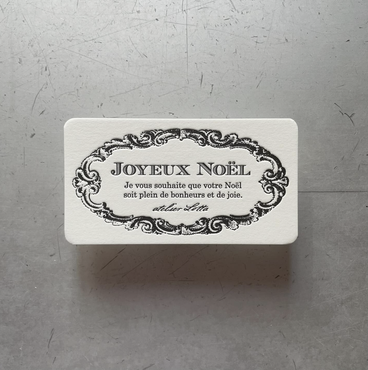 クリスマスの挨拶カードのようなデザインの白いカード。フランス語で『メリークリスマス』と書かれ、その下に幸せと喜びを願うメッセージが記載されている。