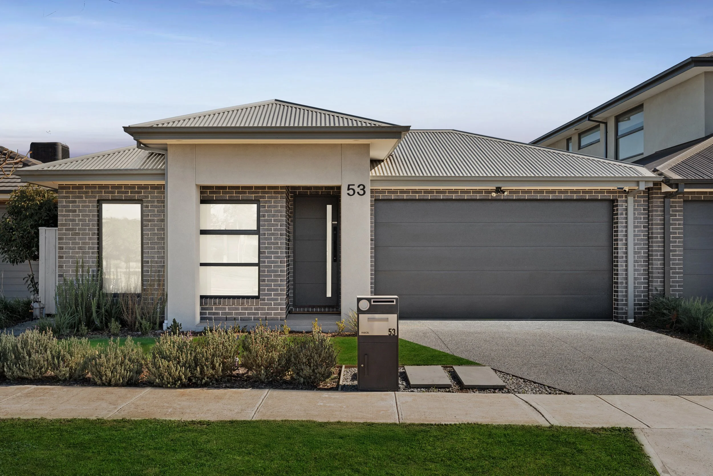 Modern single-family house with a brick and stucco exterior, gray garage door, front door, lawn, landscaped garden, and mailbox.