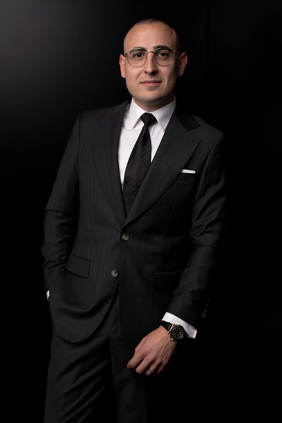 Man in a dark suit with glasses and a watch