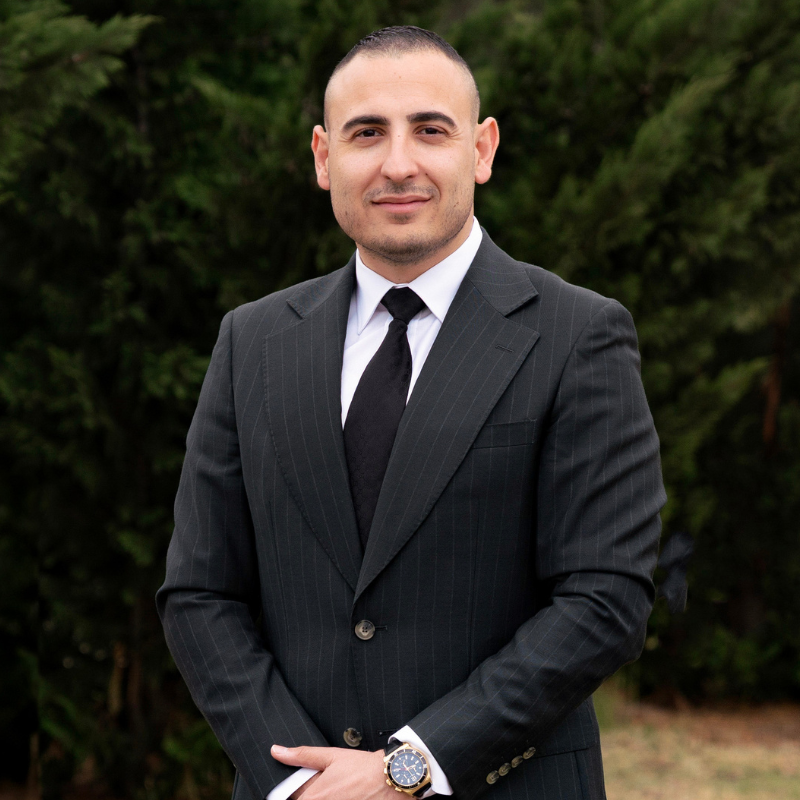 Man in a dark suit with glasses and a watch