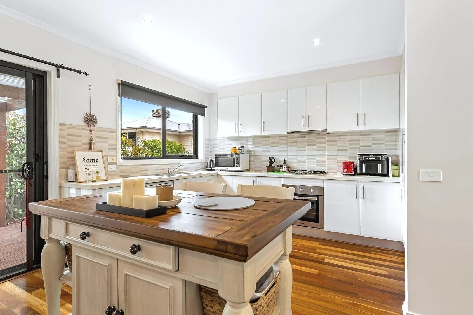 Modern kitchen with white cabinetry, wooden countertops, and hardwood floors. Includes a kitchen island, window, microwave, stove, toaster, coffee machine, and candles on the island.