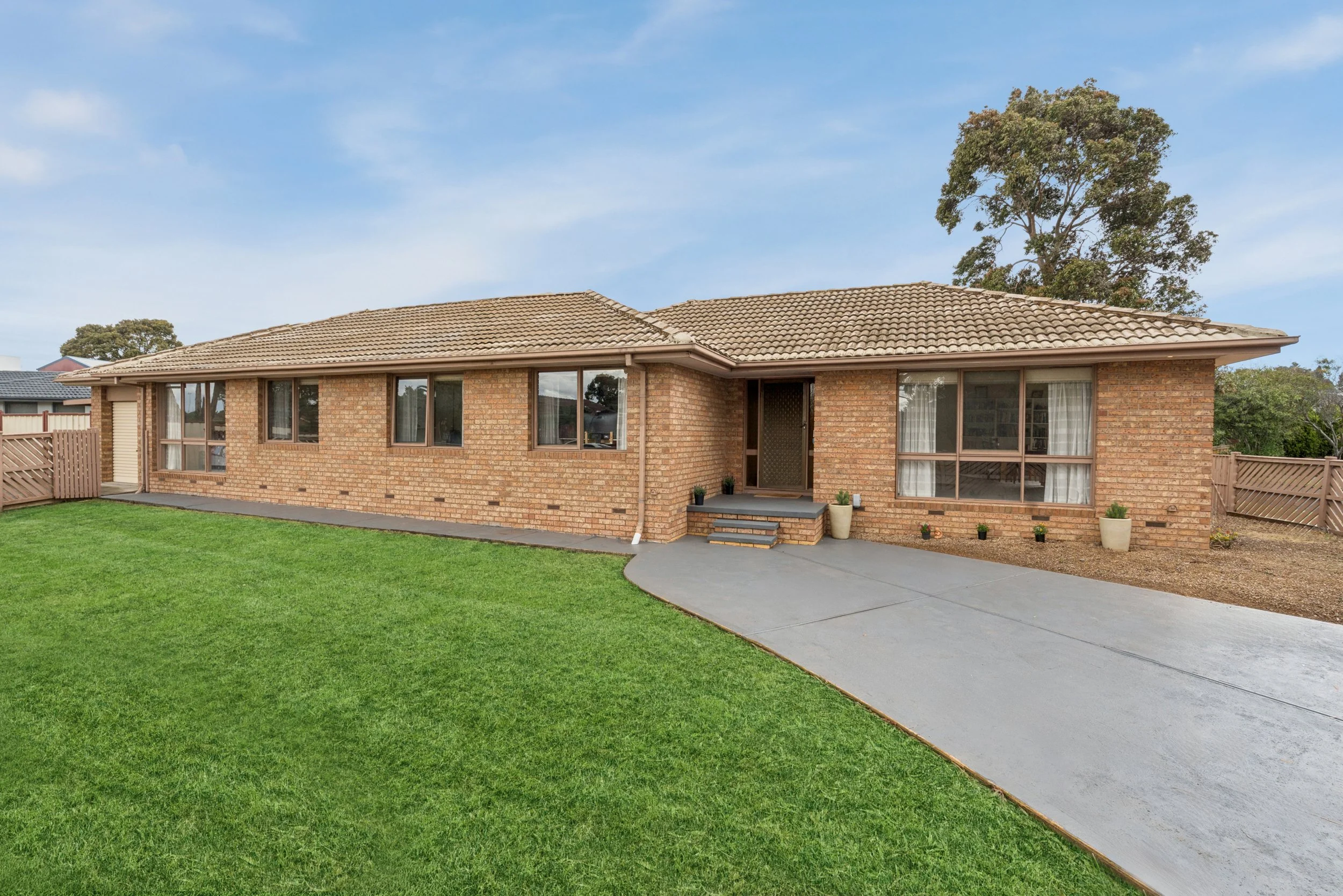 Single-story brick house with a tiled roof, large front windows, a concrete driveway, and a well-maintained lawn.
