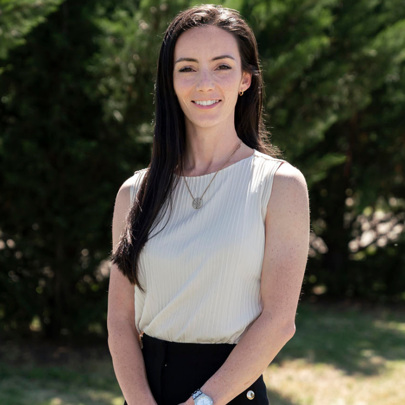 Smiling woman with long dark hair wearing a brown dress, against a black background.