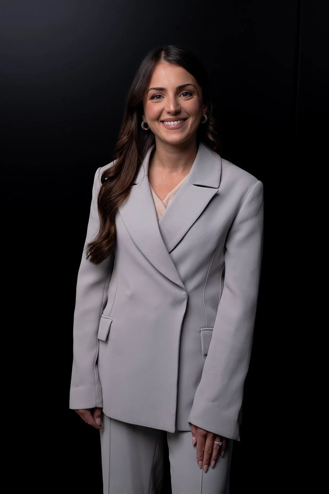 Smiling woman in gray suit against black background.