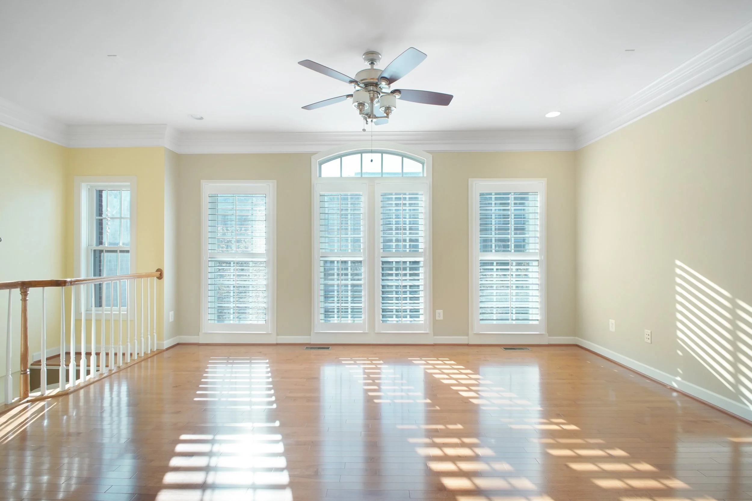 Bright living room with large windows, hardwood floors, a ceiling fan, and light yellow walls.
