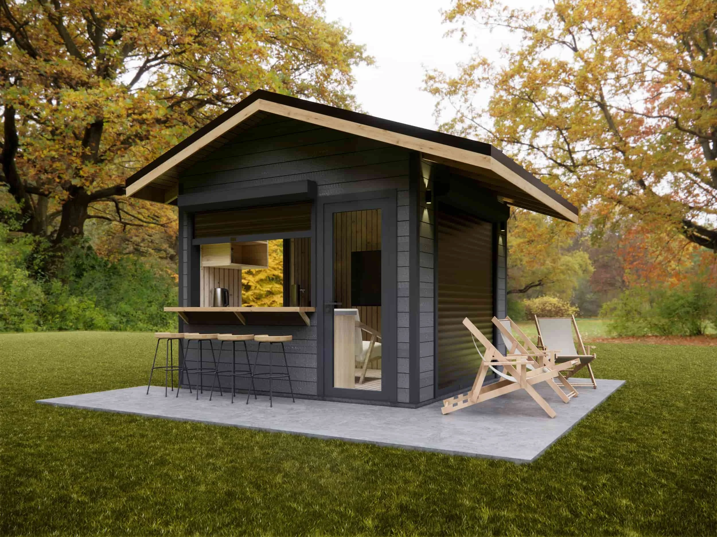 Small modern black wooden cabin with a sloped roof, outdoor bar area with barstools, and two wooden lounge chairs on a concrete patio, surrounded by trees with fall foliage.